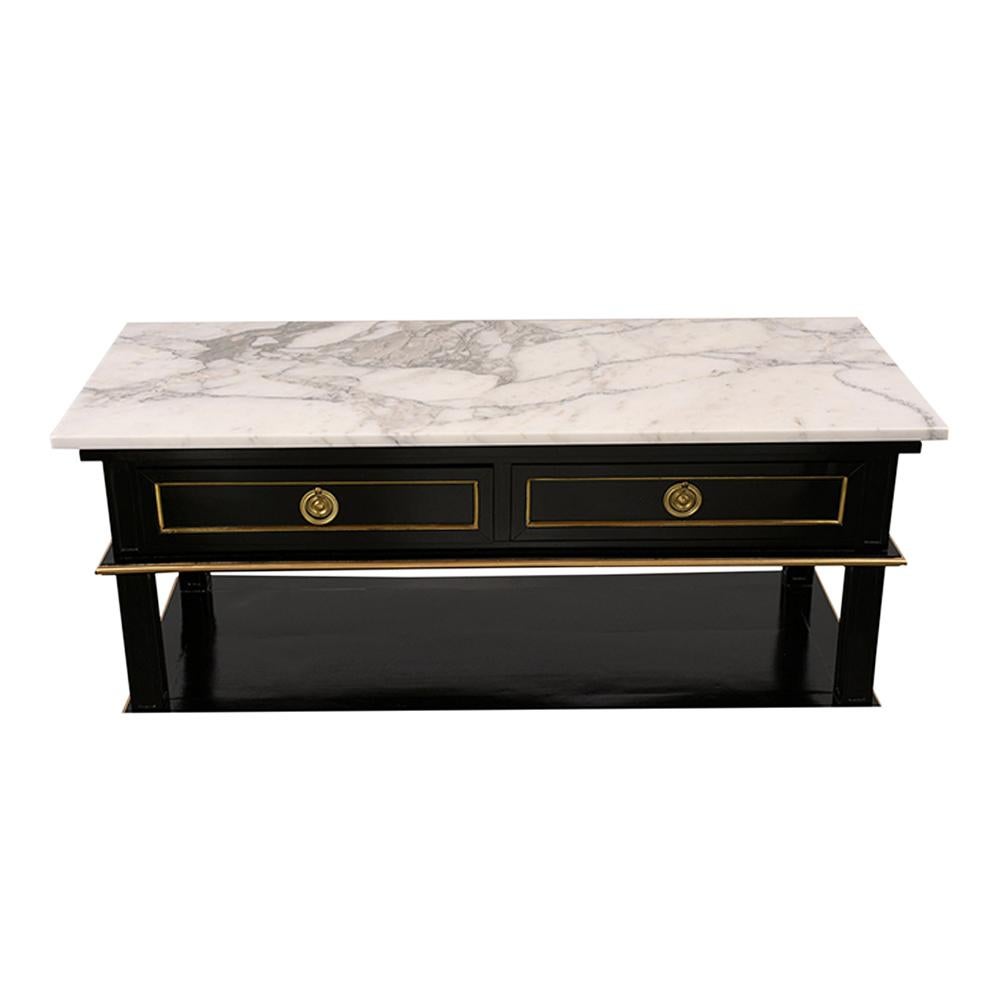 This Louis XVI style Carrara marble-top console table has an ebonized base with gilt decoration in the Louis XVI fashion. The console has a white marble top with grey veins, two shelves each with gold gilt around the trim, and 2 drawers with