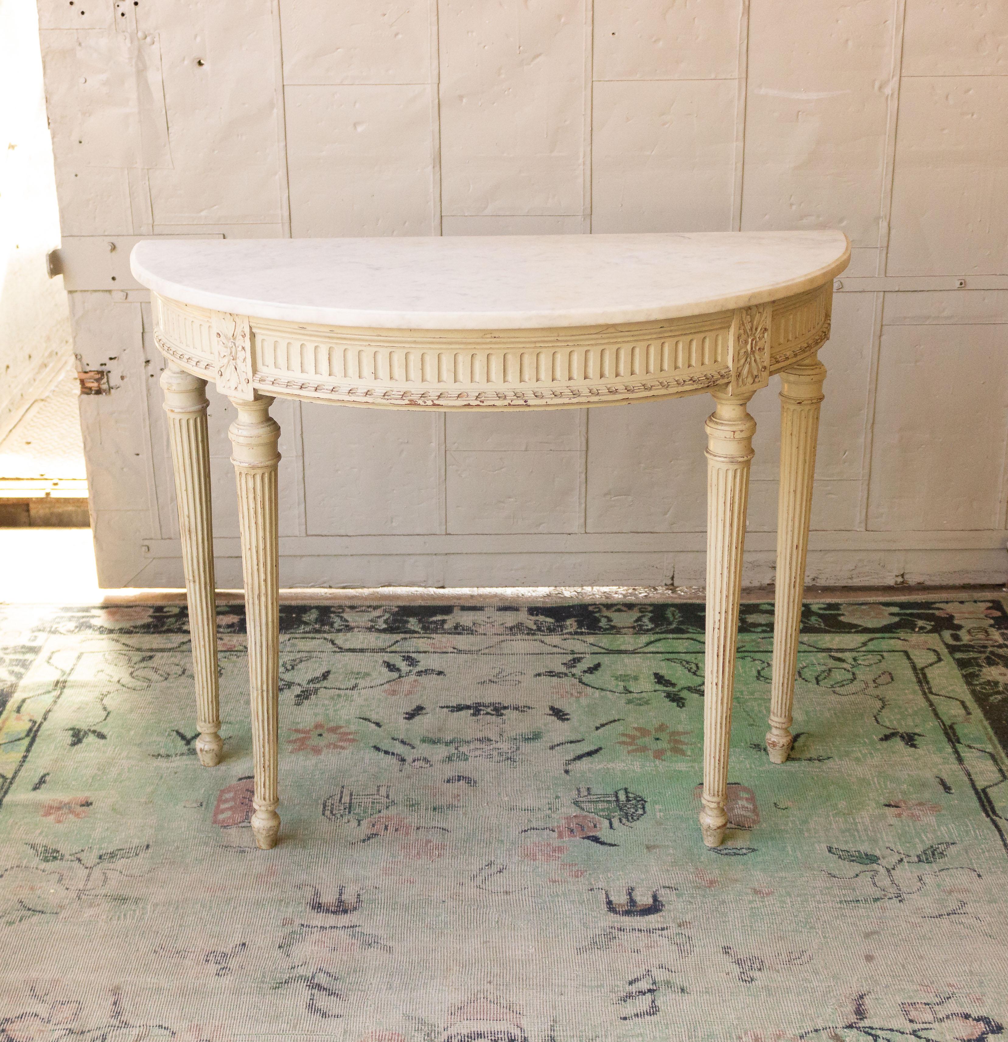 This French early 20th-century Louis XVI style painted wood console exudes elegance and sophistication, with intricate details and classic design elements. The console features an original marble top that has developed some age spots, adding