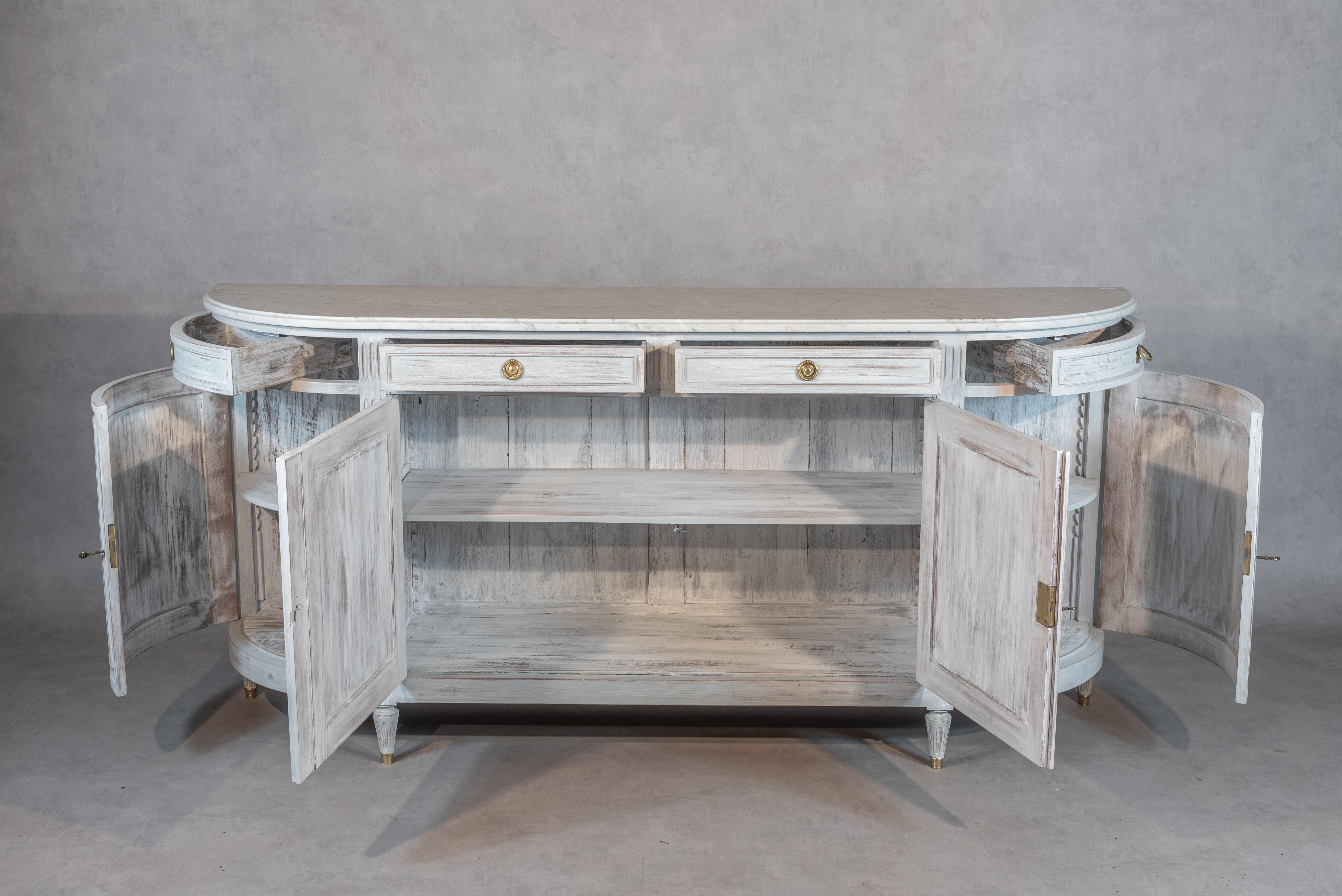 This stunning French Louis XVI style enfilade from the Mid-20th Century is a true work of art. Meticulously refurbished to its former glory, this enfilade has been professionally sanded, bleached, and painted in a gorgeous white patina that