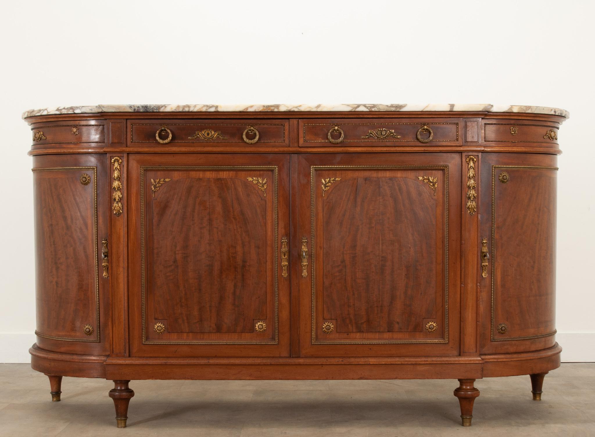 A striking demi lune enfilade from France, circa 1870, with a busy, shaped, multi-colored stone top and wonderful ormolu throughout. The apron houses two proper drawers and two rounded faux drawers. A pair of laurel wreath drop ring pulls open each