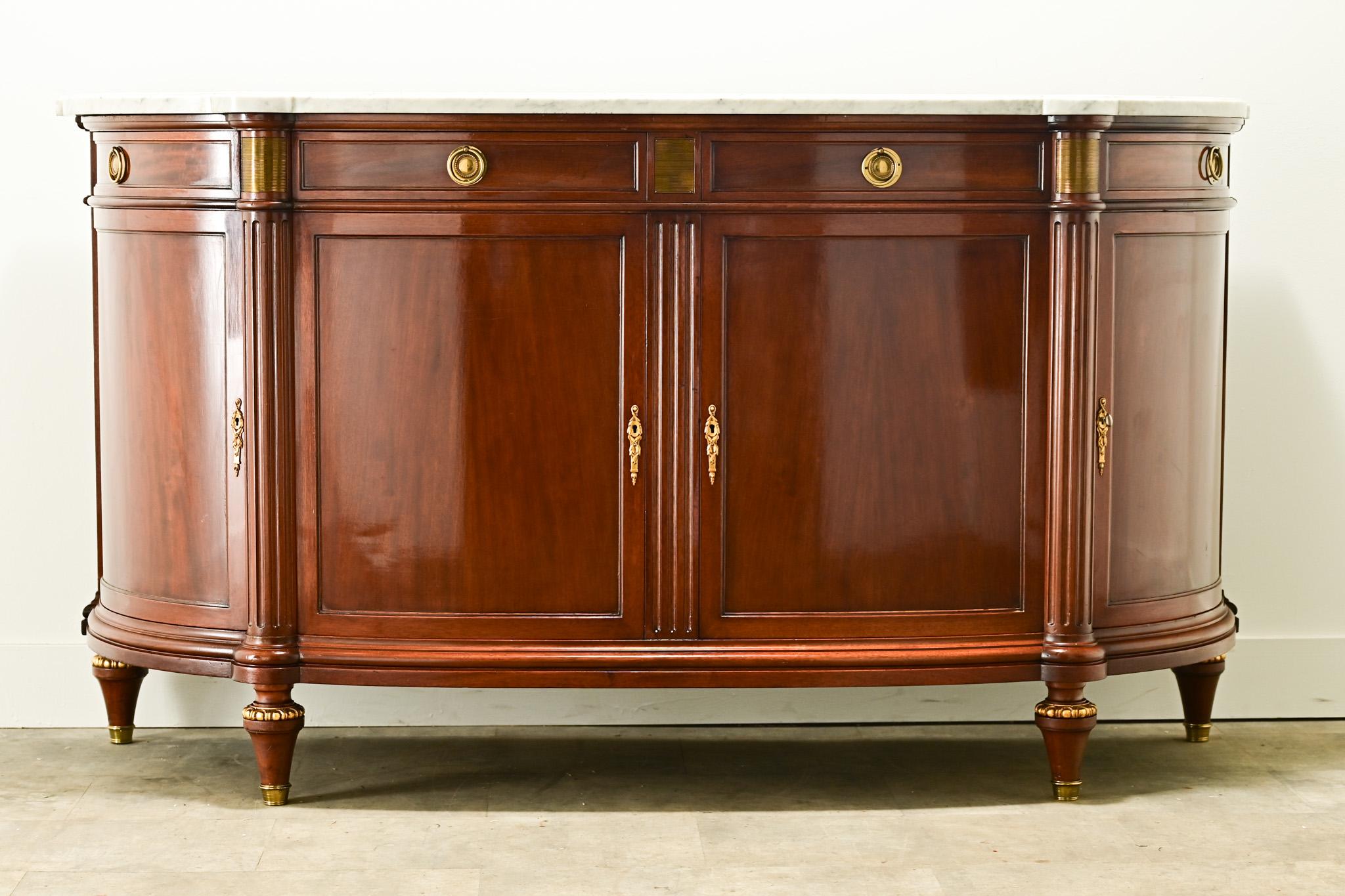 A refined Louis XVI style demilune shaped enfilade made in France. The original shaped white marble top rests over its mahogany base. The center of the cabinet has two drawers that open with brass ring pulls and two paneled doors, flanked with