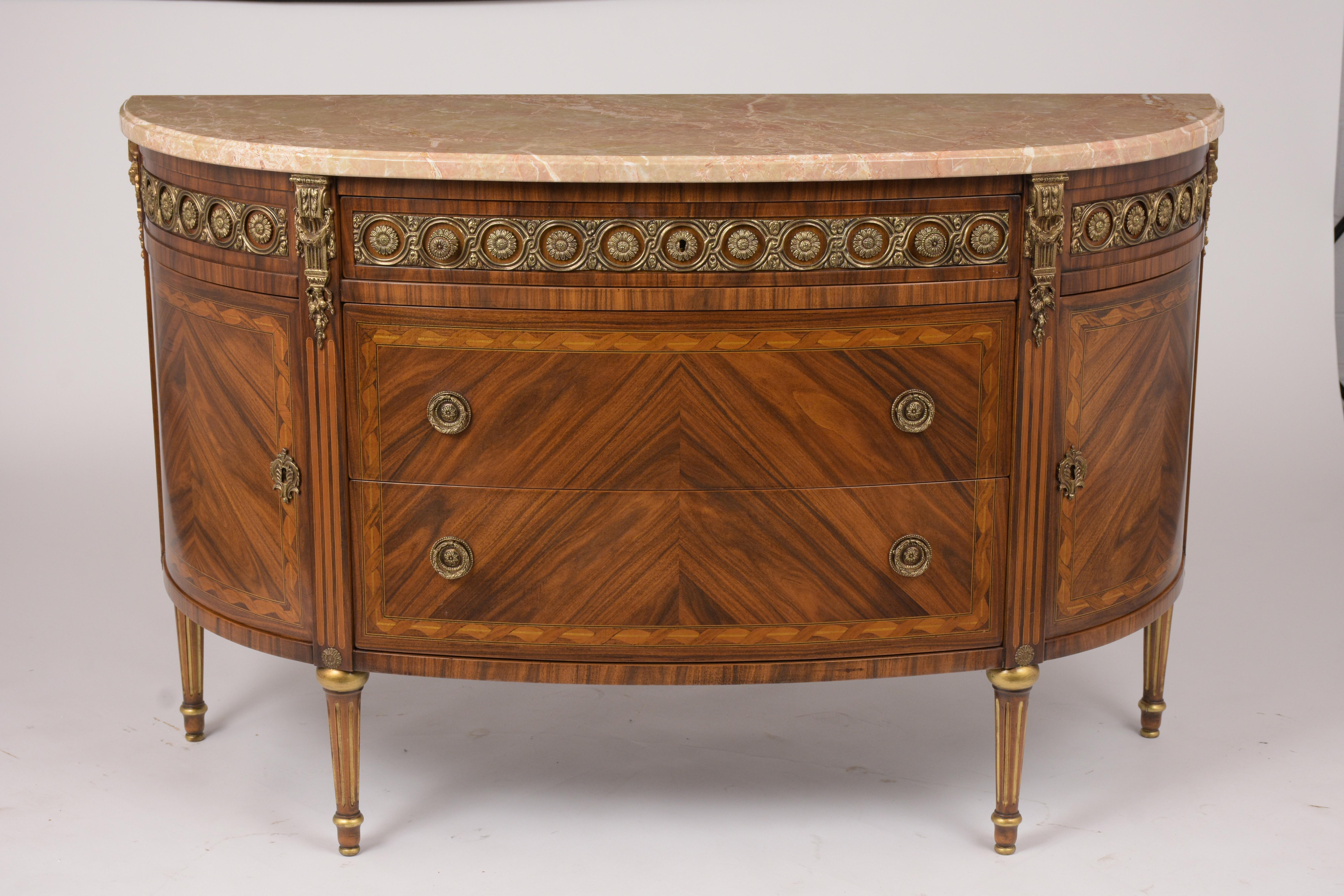 This French Louis XVI Style Demilune Server features a bevel marble top, marquetry design, and beautiful inlaid details throughout the piece. The buffet comes with an intricately detailed brass accent gallery along the top and large top drawer that