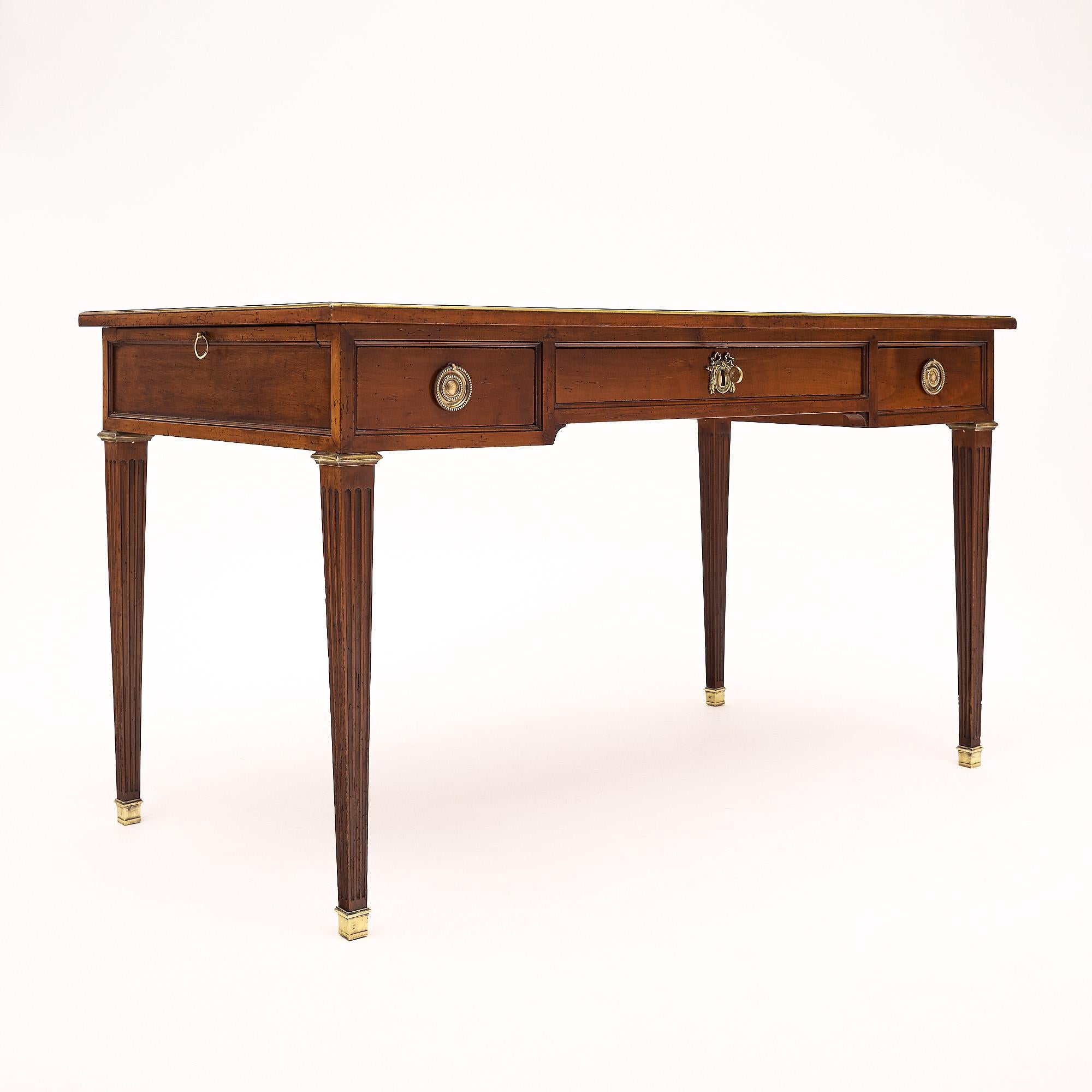 French desk made of solid cherry wood and hand rubbed with a beeswax finish. The writing table boasts a light brown leather top, 2 pullout leaves lined with leather as well, three dovetailed drawers with original brass hardware, fluted square