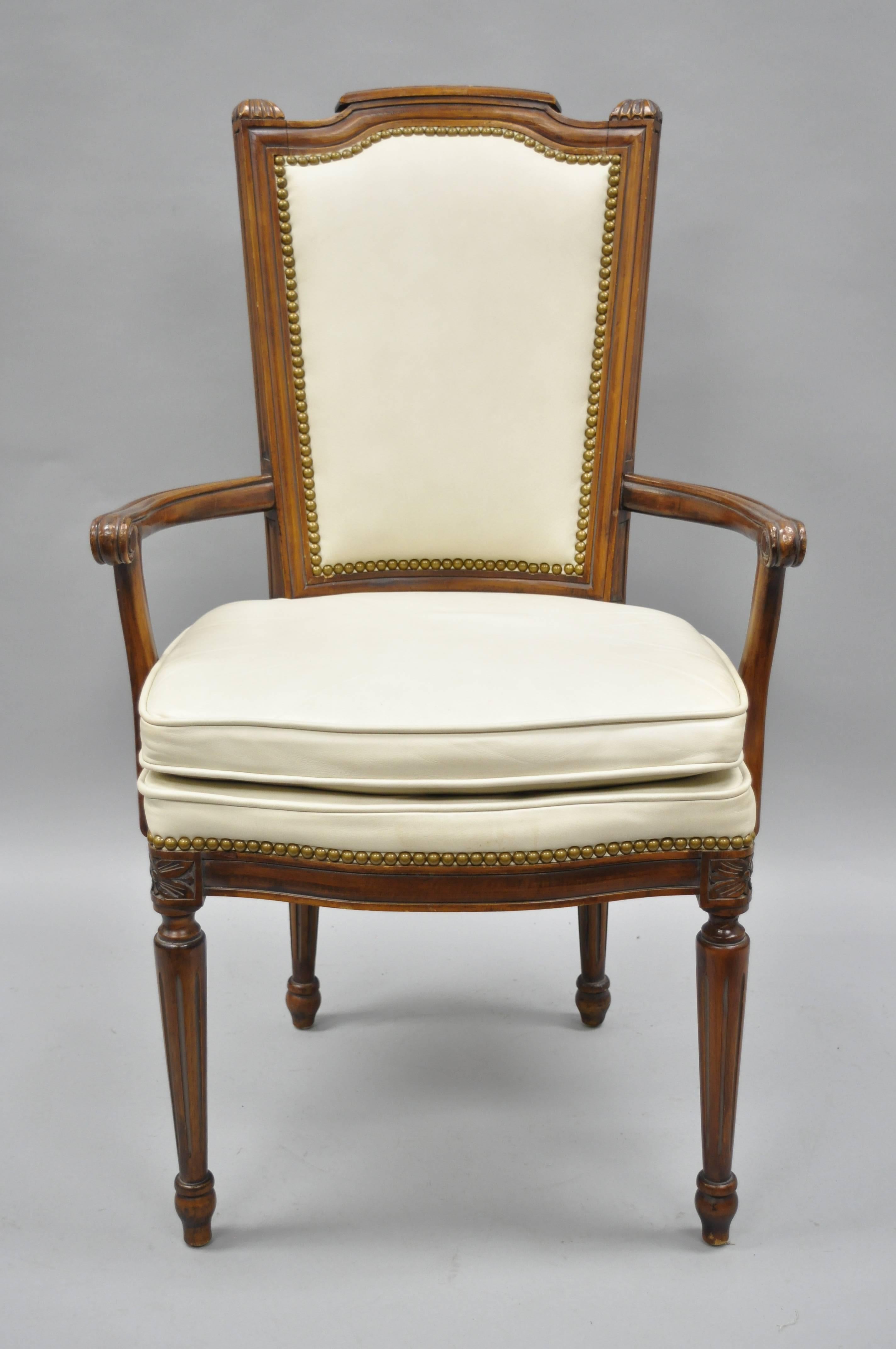 Set of eight French Louis XVI style walnut dining chairs with leather upholstery. Listing includes six side chairs, two armchairs, off white leather upholstery, nailhead trim, solid wood construction, tapered legs, and quality American