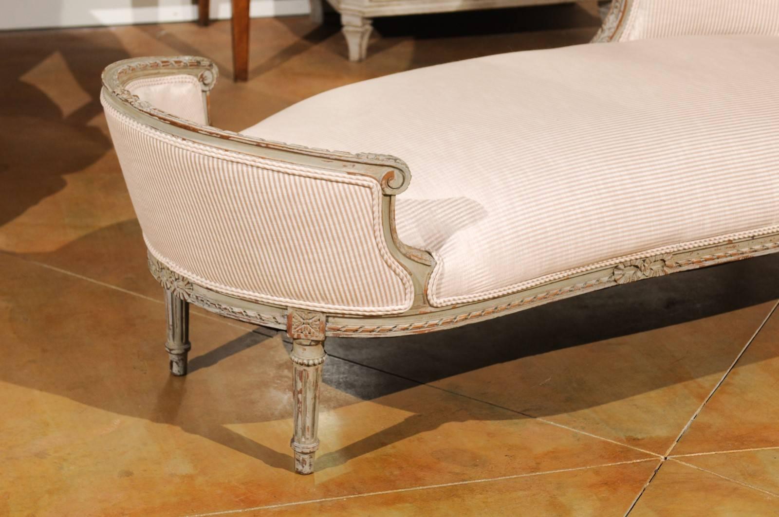 A French Louis XVI style painted and carved wood daybed from the 19th century, with twisted ribbon motifs, acanthus leaves and striped fabric. This French painted 'duchesse en bateau' features spectacular carved details on its entire structure. The