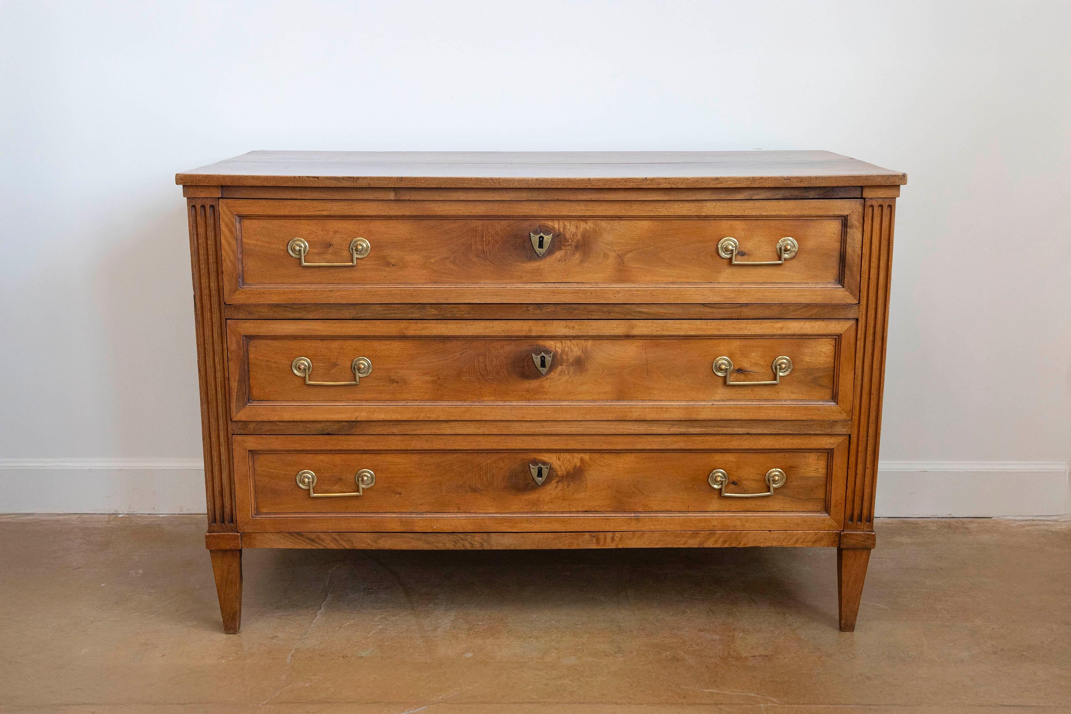 Commodo francese in noce in stile Luigi XVI dell'inizio del XIX secolo con tre cassetti, montanti laterali scanalati e maniglie originali. Creata in Francia nei primi anni del XIX secolo, questa commode in noce presenta un piano rettangolare a