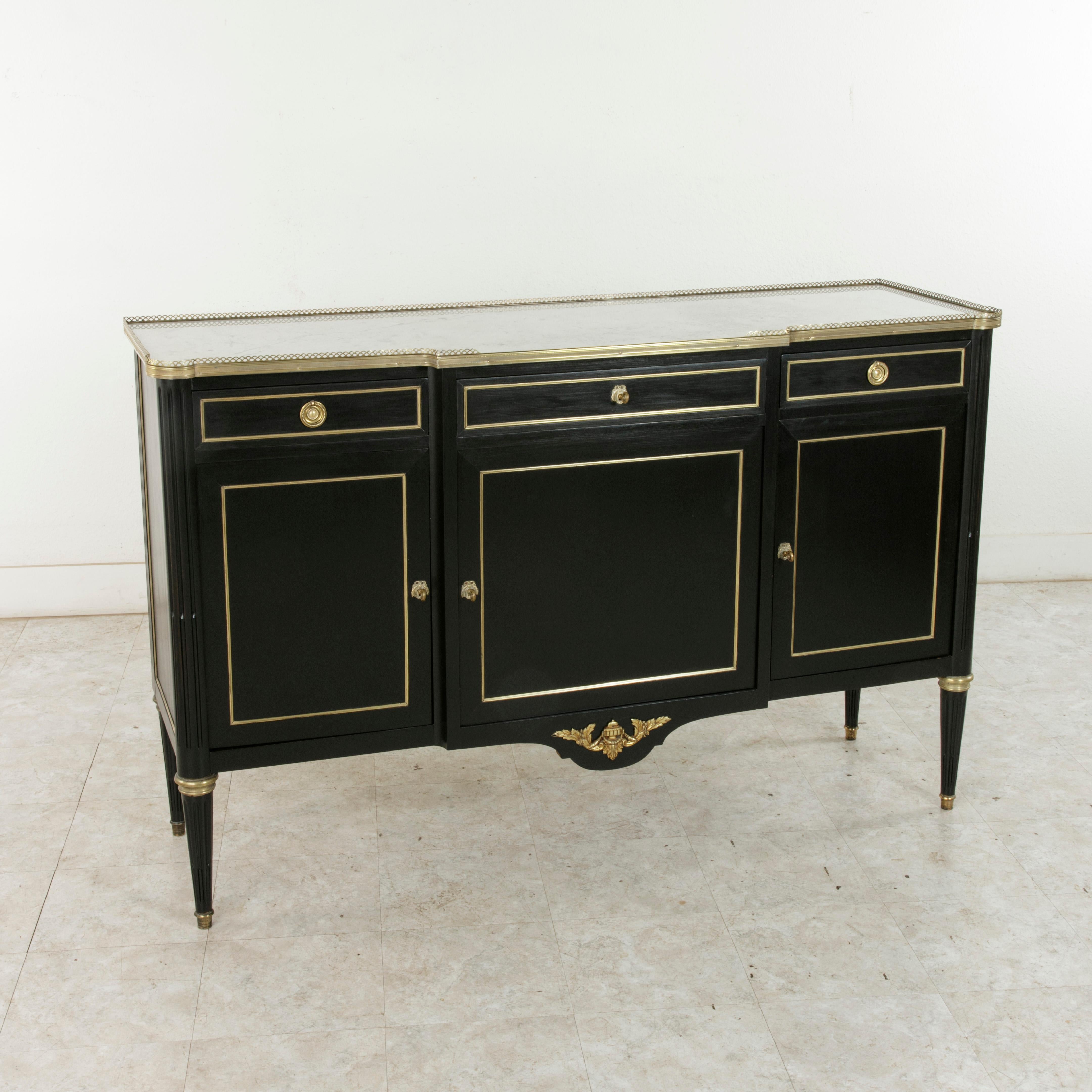 This French Louis XVI style enfilade or sideboard from the mid-20th century features an ebonized mahogany facade with a white marble top. Bronze trim frames the door and drawer panels as well as the side panels, and a bronze gallery surrounds the