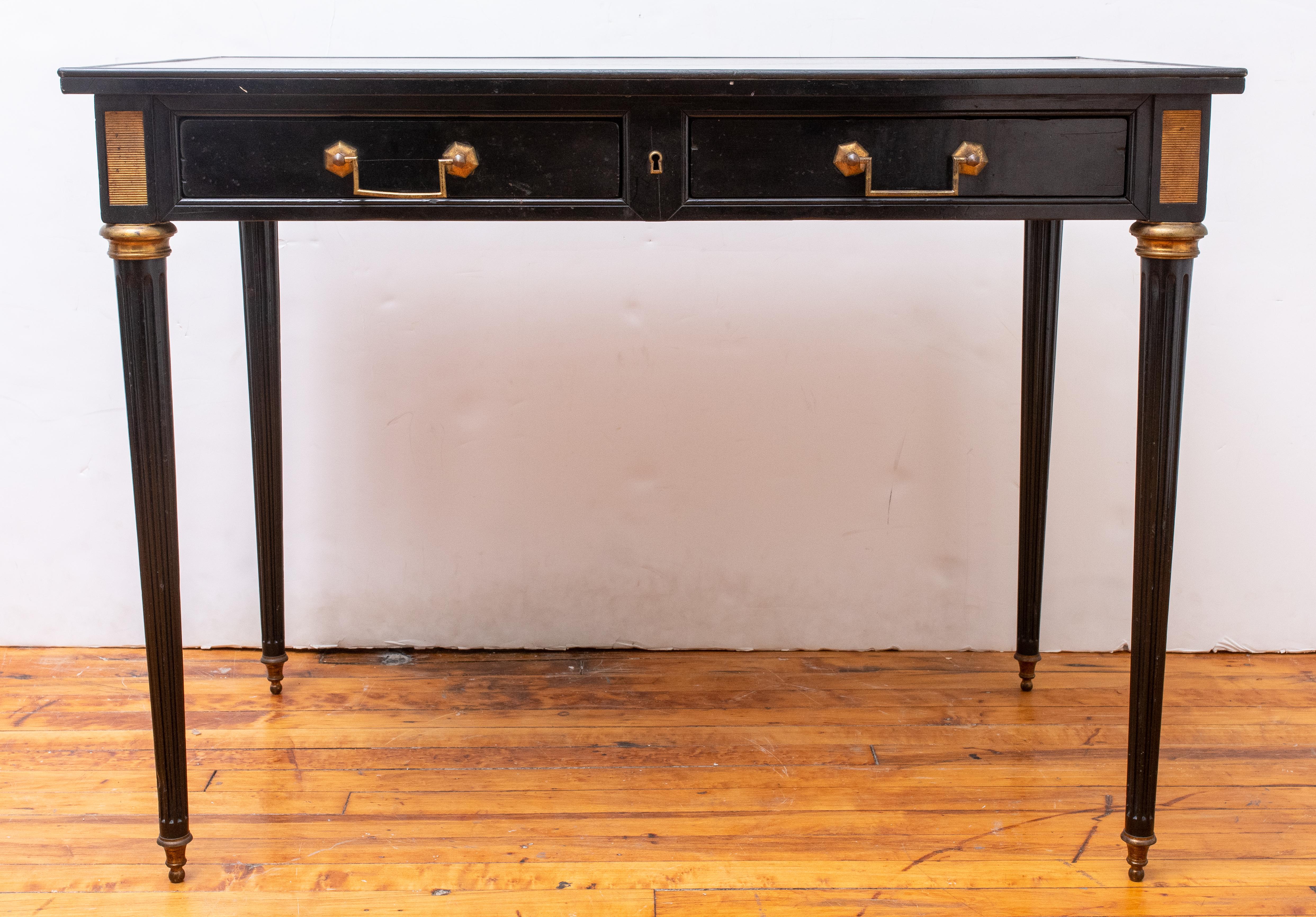 French Louis XVI Style ebonized and gilt metal-mounted bureau plat in the manner of Jansen, rectangular top above two drawers, the corners headed by paterae, the tapering fluted columnar legs terminating in toupie sabots.

