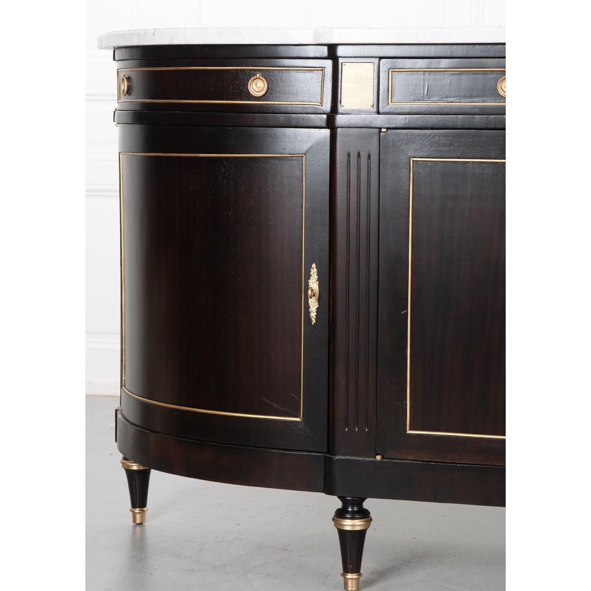 French early 20th Century mahogany demilune enfilade has recently been ebonized using many layers of ebony stain. Its original, shaped white marble top sits over the demilune base. All the hardware has been cleaned making the brass stand out against