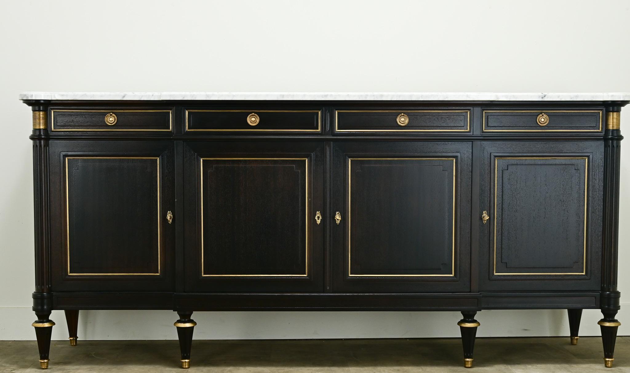 A large ebonized mahogany breakfront enfilade in the classic Louis XVI style. The original marble top is shaped to fit its base with beveled edges. There are four drawers trimmed with brass and brass ring pulls. Four paneled door fronts are also
