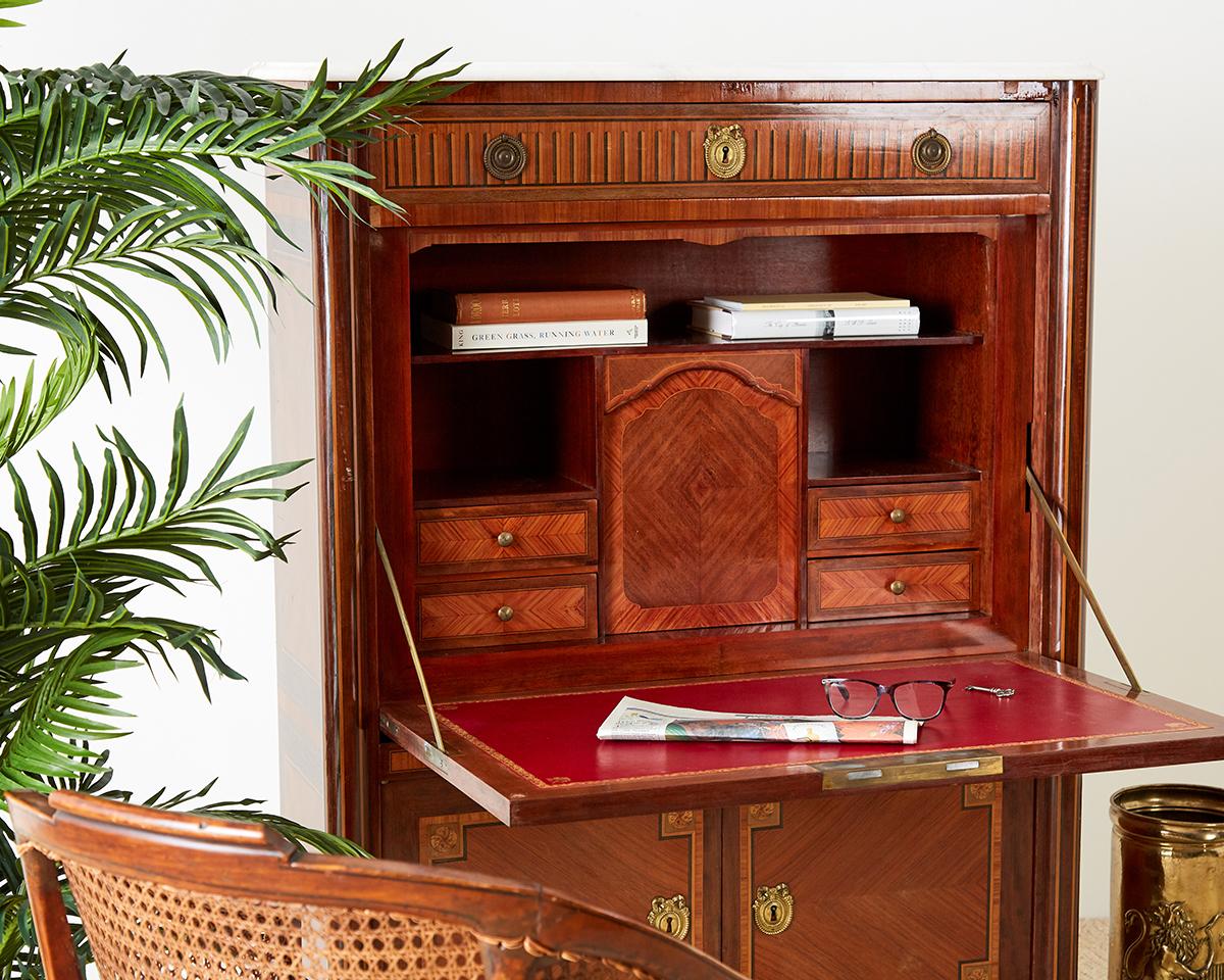 Fantastic fall front secretaire abattant desk made in the French Louis XVI taste. Features a large drop leaf style desk with a red tooled leather surface. The case is decorated with beautiful marquetry inlay on all three sides and on each drawer and