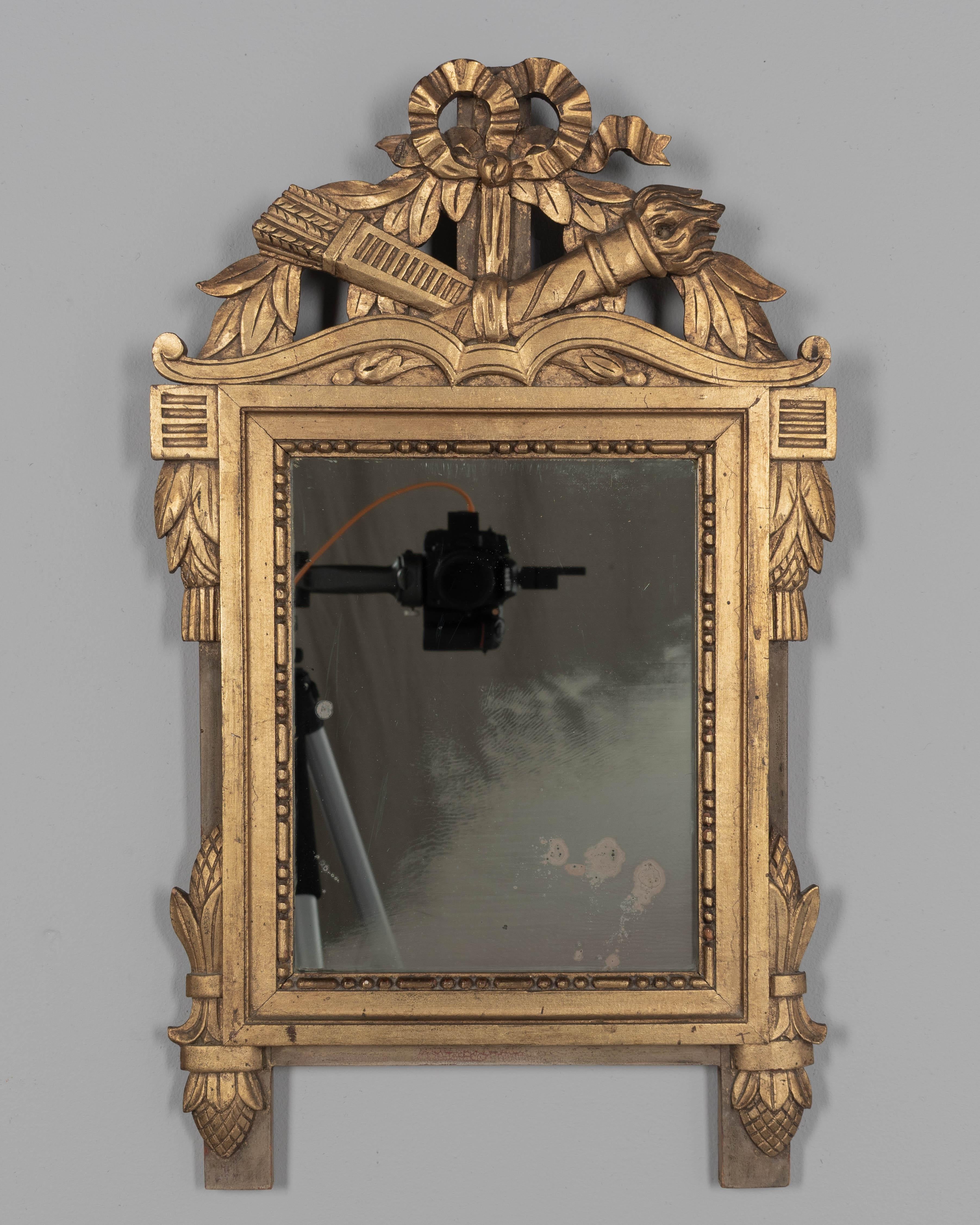 A Louis XVI style French Provençal giltwood mirror. Hand carved crest with ribbons, garlands, torch and quiver. Gilt is in good condition with bright finish. Mirror is original with spots and fogging.  No restorations. Circa 1950s
Overall