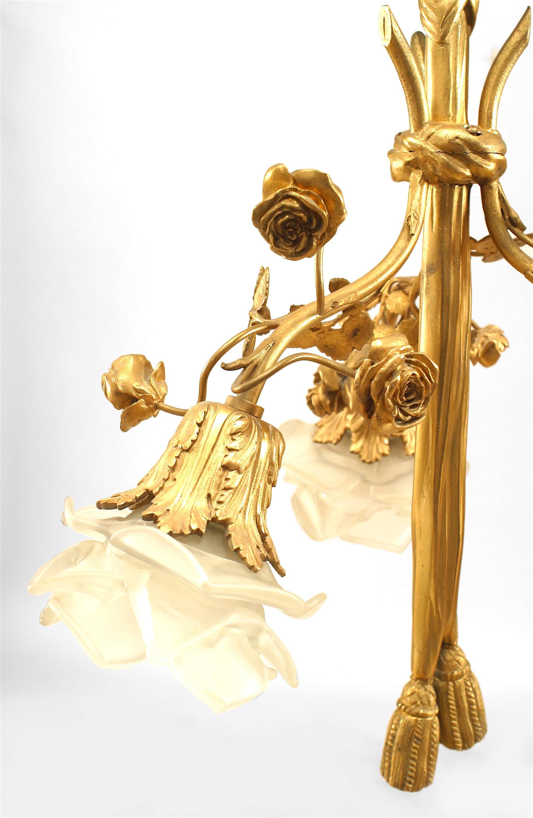Lustre en bronze doré de style Louis XVI, orné de fleurs et centré d'un drapé se terminant par des glands, avec 3 bras se terminant par des abat-jour en verre.
