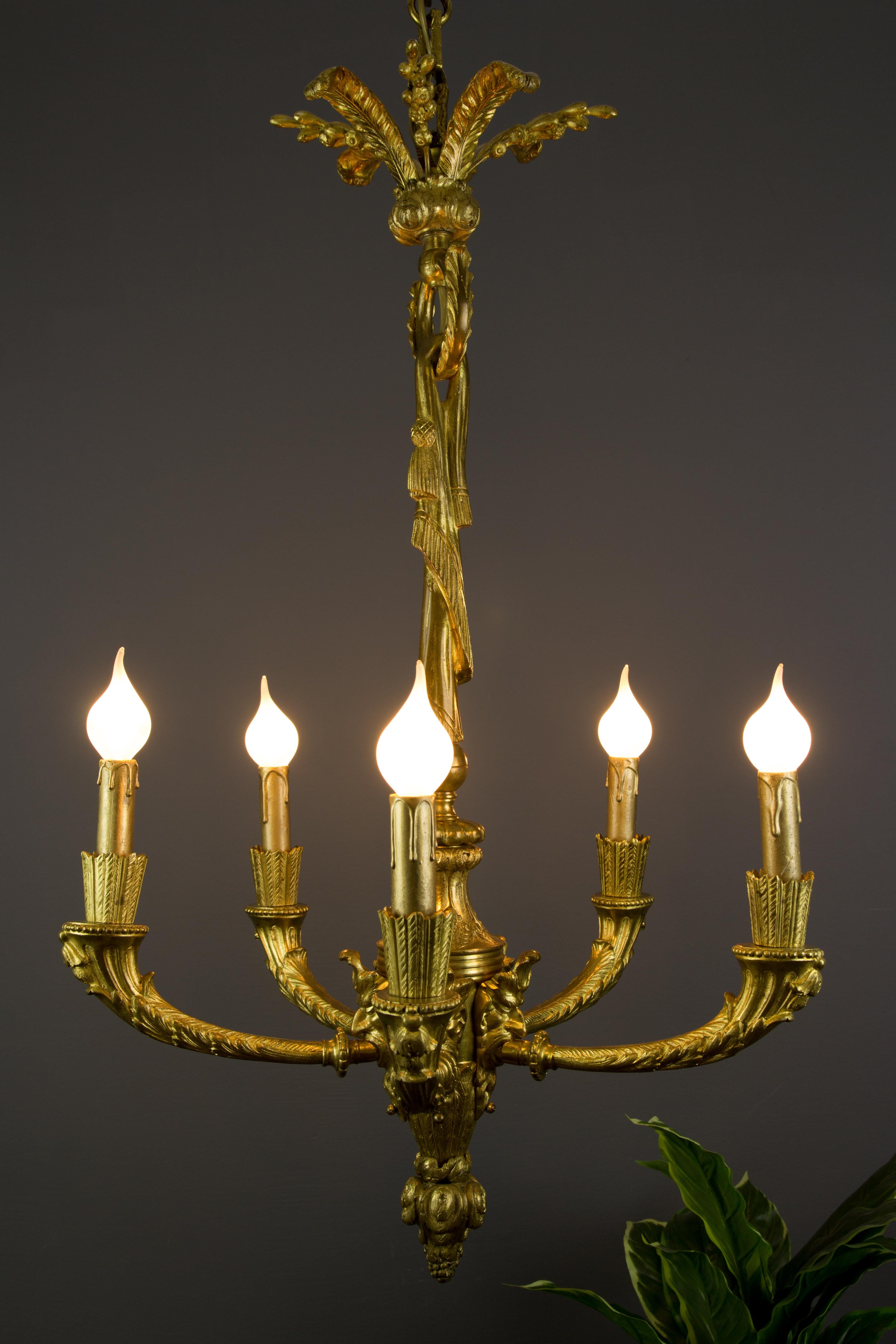 Elegant French Louis XVI style gilt bronze five-light electrified chandelier from the late 19th century. Each arm is held by a head of Bacchus and decorated with foliate motifs. The central support is draped with a bronze fringe fabric, on top