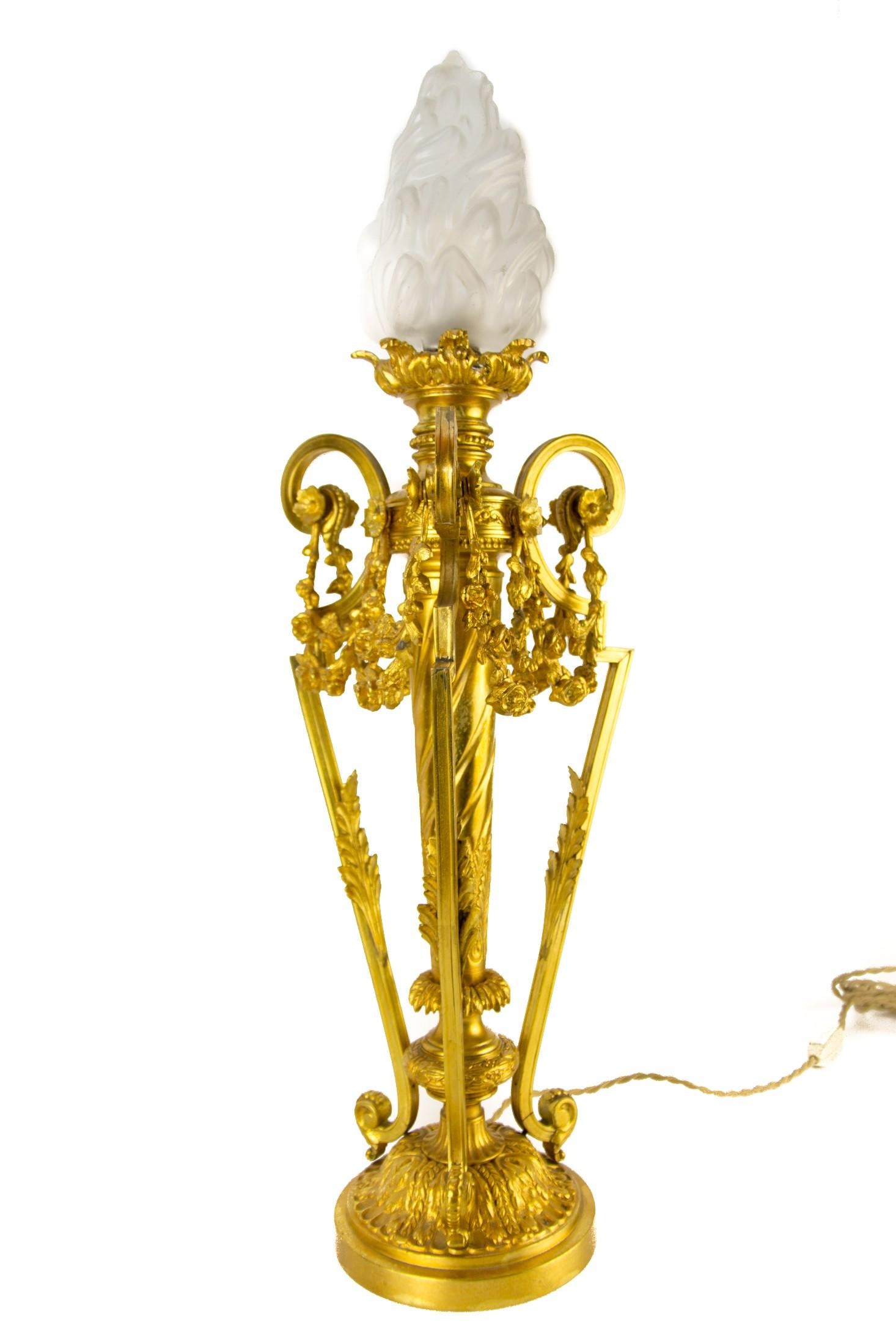 French Louis XVI style gilt bronze newel post lamp with frosted glass flame shade and original E27 socket, France, 1920s.
Richly decorated with bronze decors in a form of acanthus leaves and floral garland drapes.
Generally, in very good