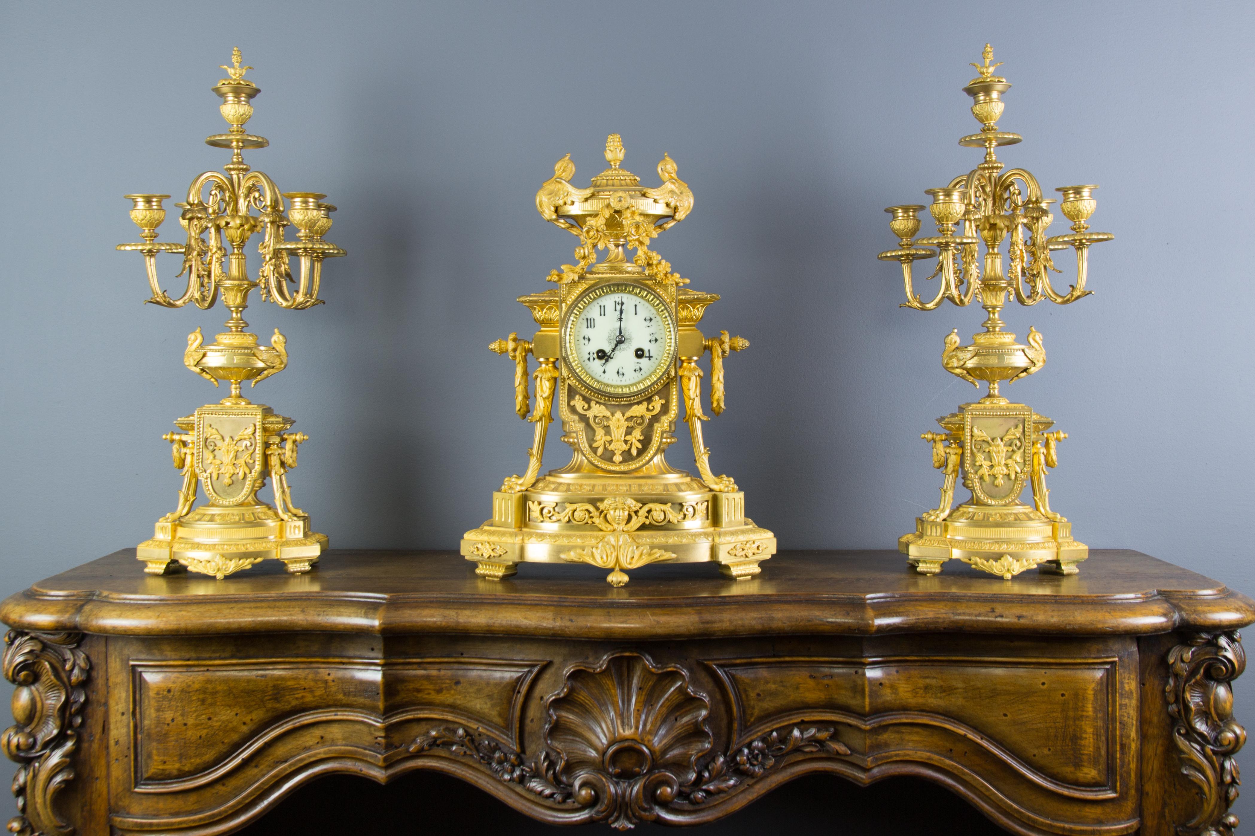 Stunning and very fine quality French late 19th century Louis XVI style gilt bronze mantel clock and a pair of five-light candelabra; the mantel clock of architectural form surmounted by urn finial, flanked by two swans. The mantel clock is centered