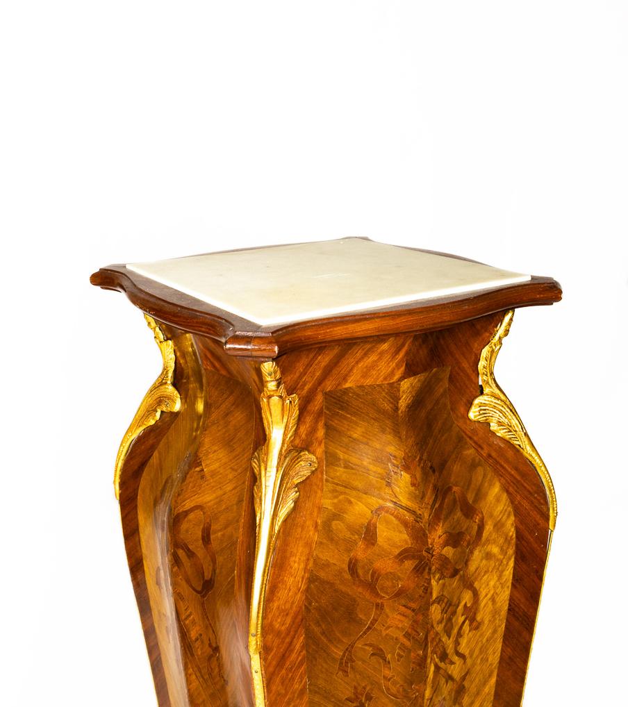Un vibrante juego de pedestales de parquetería con encimeras de mármol, caras curvas con motivos de parquetería y ornamentadas monturas de bronce dorado y patas cortas doradas. 
La decoración es expresiva a la vez que refinada, combinando el estilo