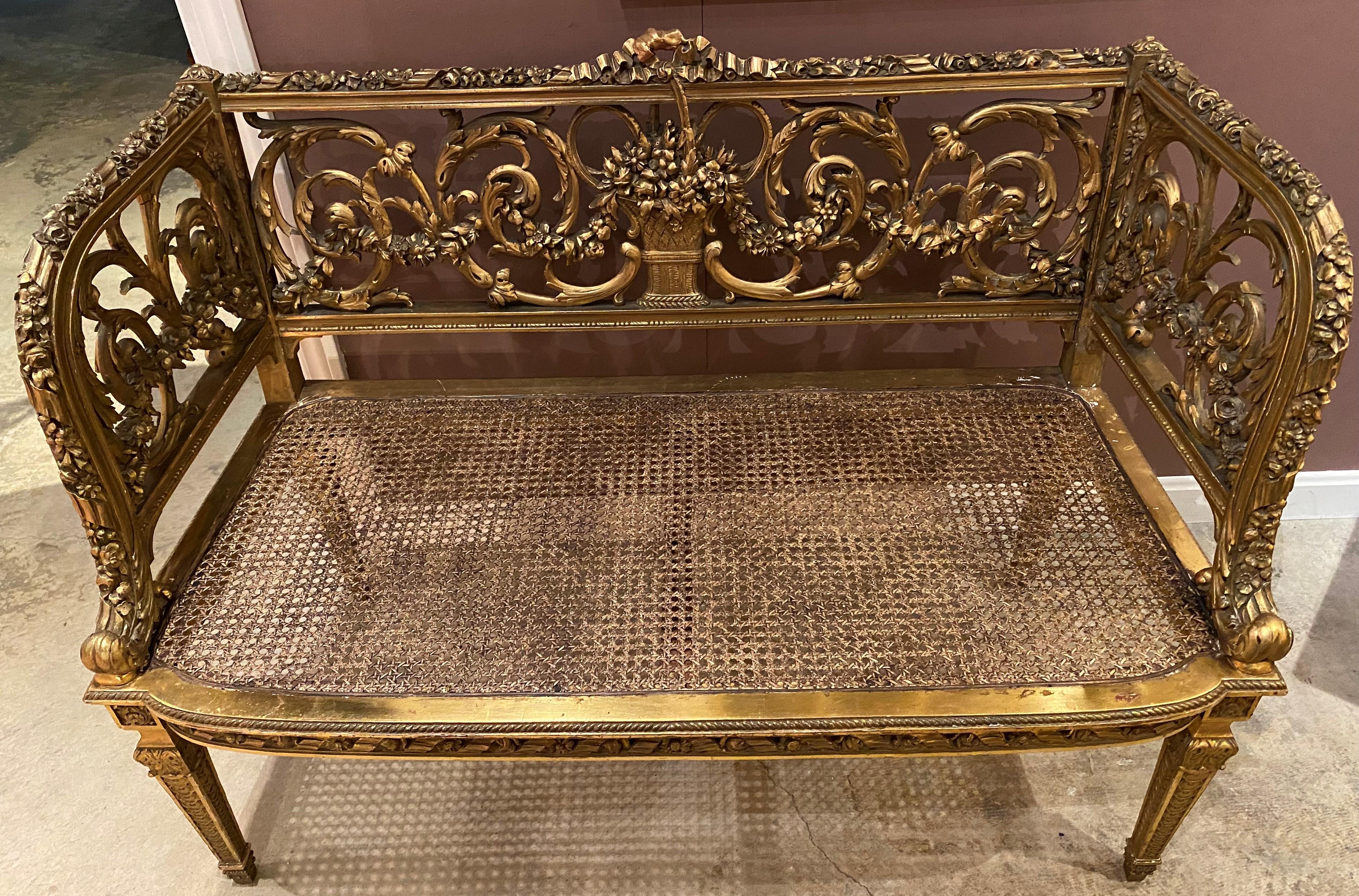 An exceptional reticulated scroll and foliate carved giltwood French Louis XVI style settee with ribbon carved crest, flower basket back decoration, and newly caned seat, all supported by four detail carved square tapered legs and a newly