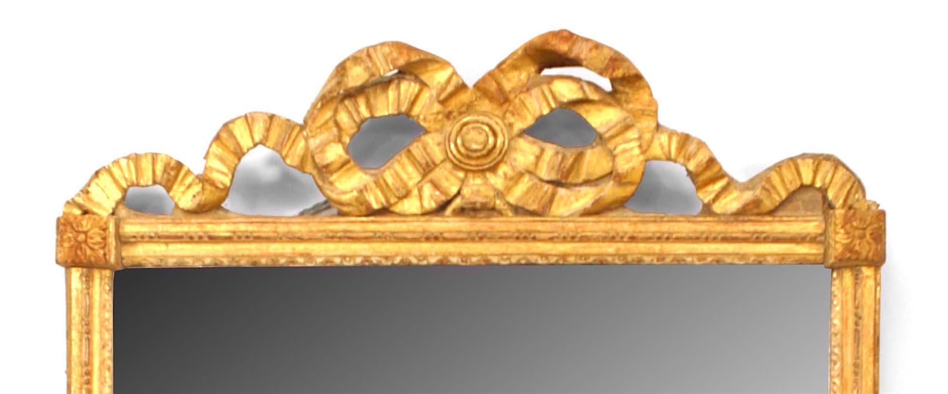 French Louis XVI-style (19th Century) giltwood wall mirror with carved filigree ribbon bow knot design pediment with original glass and raised block corners with rosette details.
