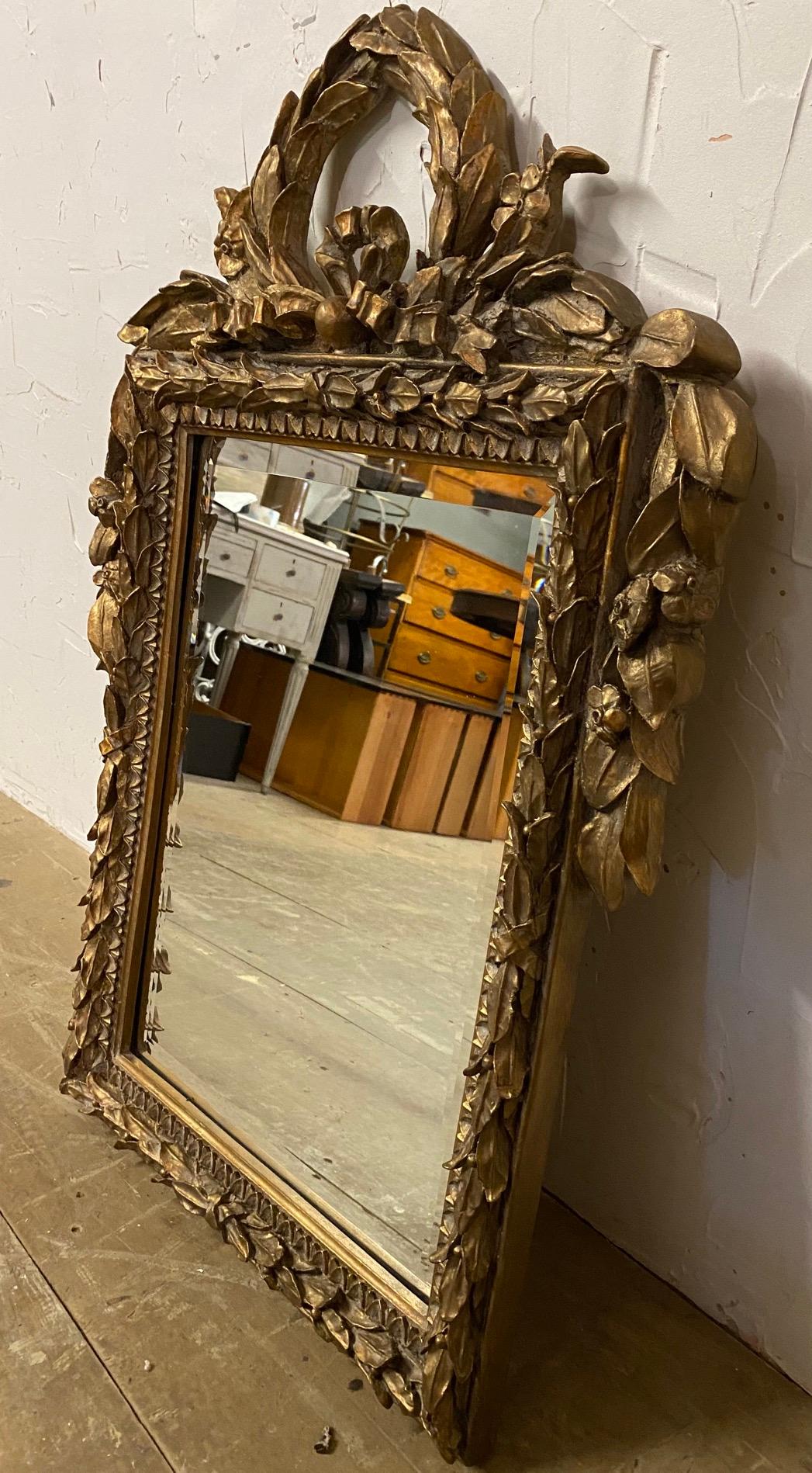 A charming vintage French Louis XVI style gilt wood wall mirror. The top has wonderful gilt carving topped with a crown of laurel wreath. This elegant mirror would make a charming addition to a living room, powder room, hallway or entry foyer. The