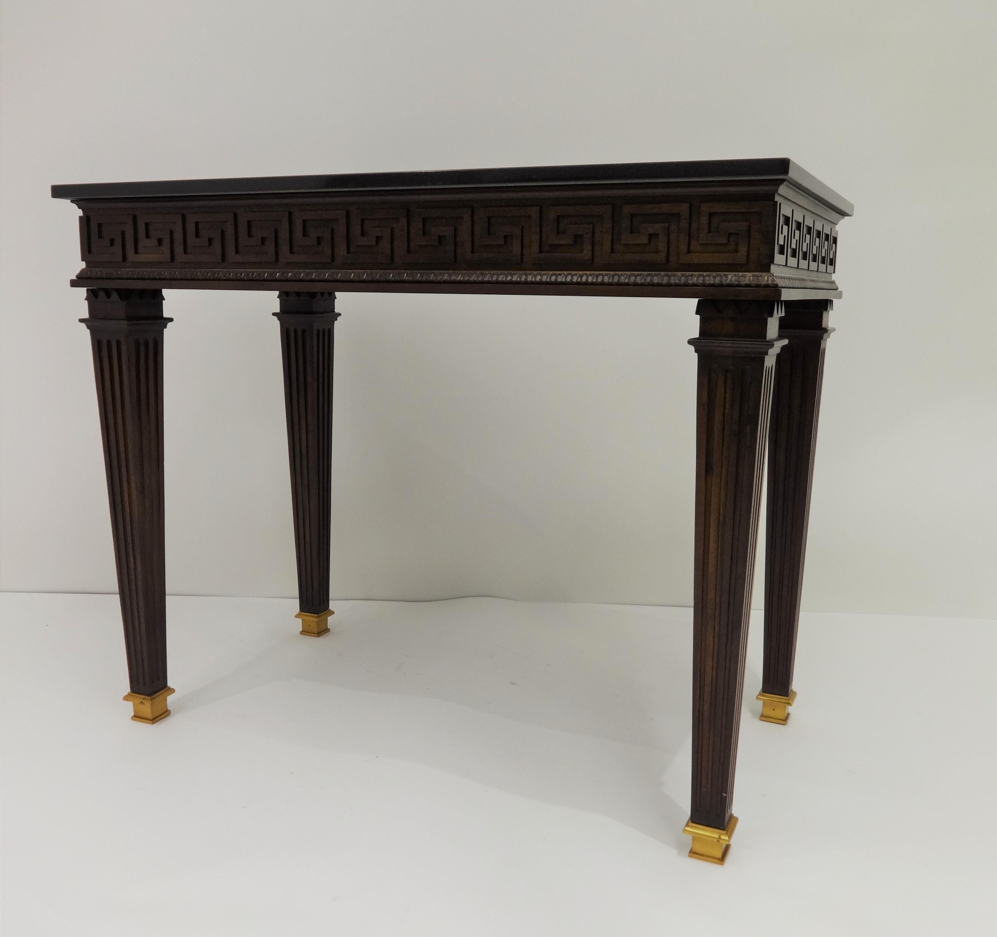 French Louis XVI style console table with Greek key design. Black granite top over a narrow frieze decorated with a carved neoclassical Greek key pattern, supported by four tapered and fluted legs ending in brass caps.