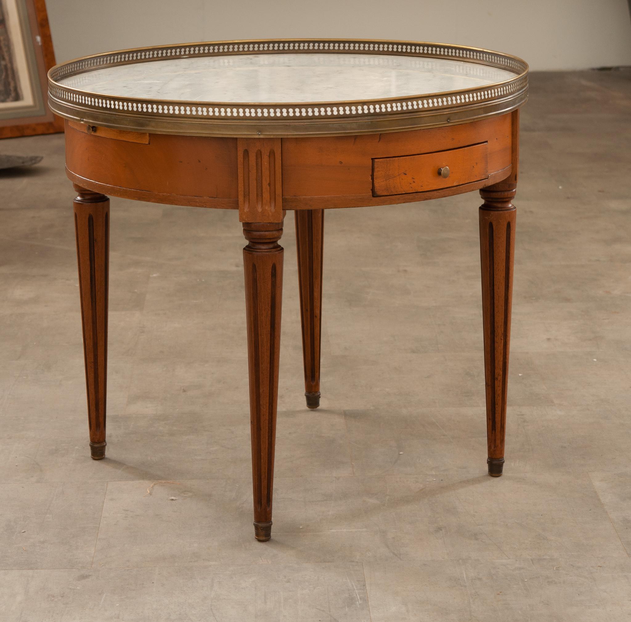 A charming French mahogany gueridon bouillotte table originally used for playing cards. A classic example of a Louis XVI style gueridon from the 20th century. Topped with white marble and surrounded by a pierced brass gallery that’s nicely