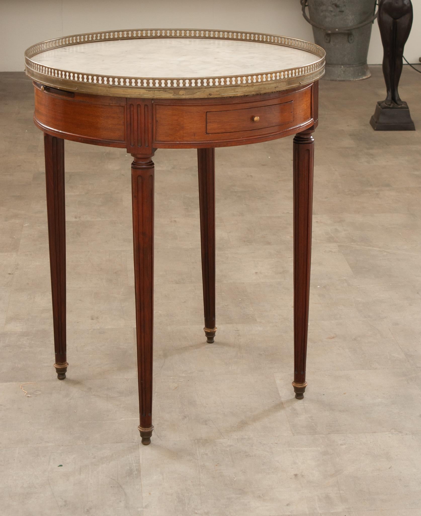 A charming French mahogany Gueridon Bouillotte table originally used for playing cards. Topped with white marble and surrounded by a pierced brass gallery that’s nicely patinated. Two drawers and two slides are housed within the apron, all with