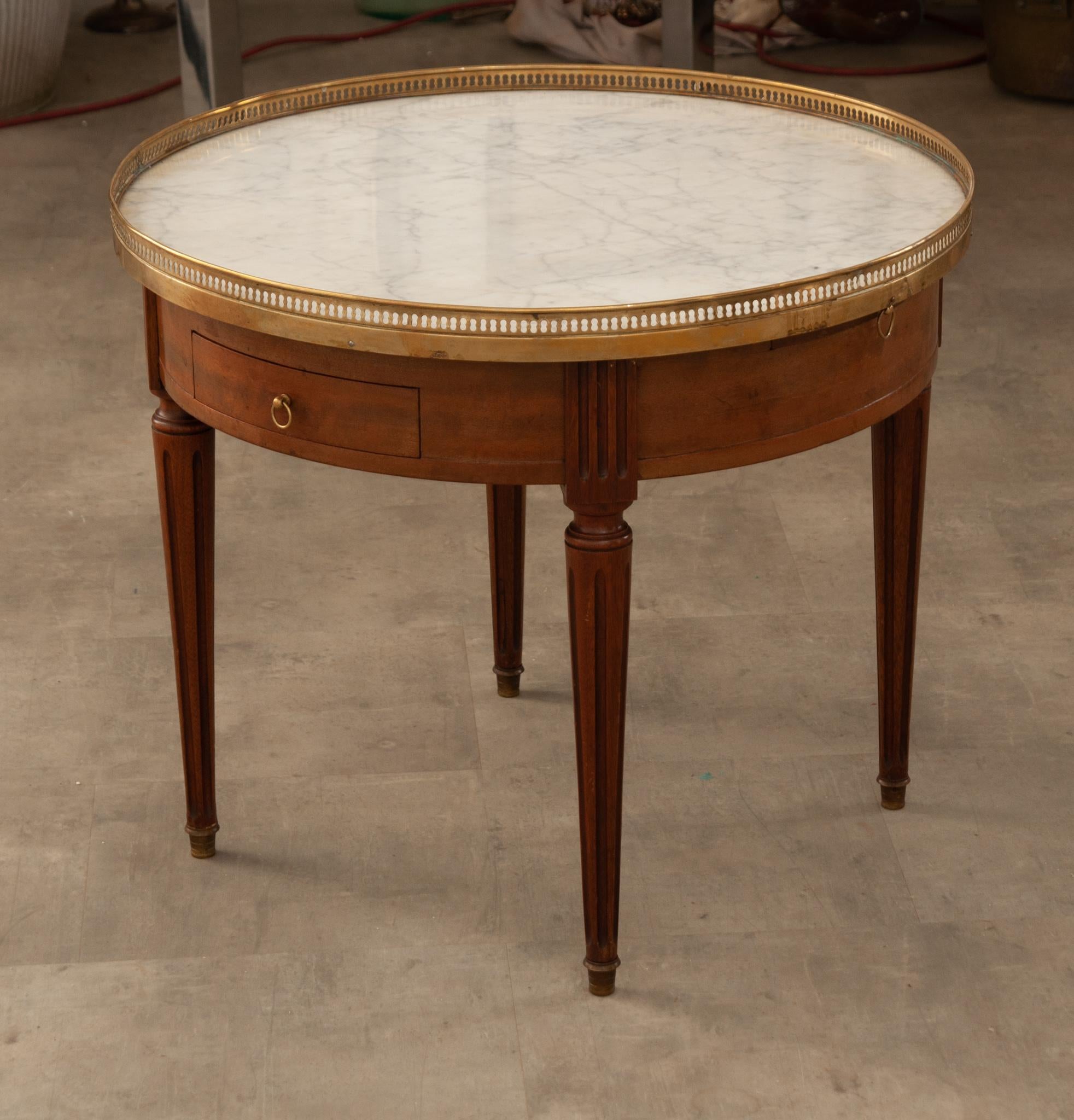 A charming French mahogany gueridon bouillotte table originally used for playing cards. A classic example of a Louis XVI style gueridon from the 20th century. Topped with white marble and surrounded by a pierced brass gallery that’s nicely