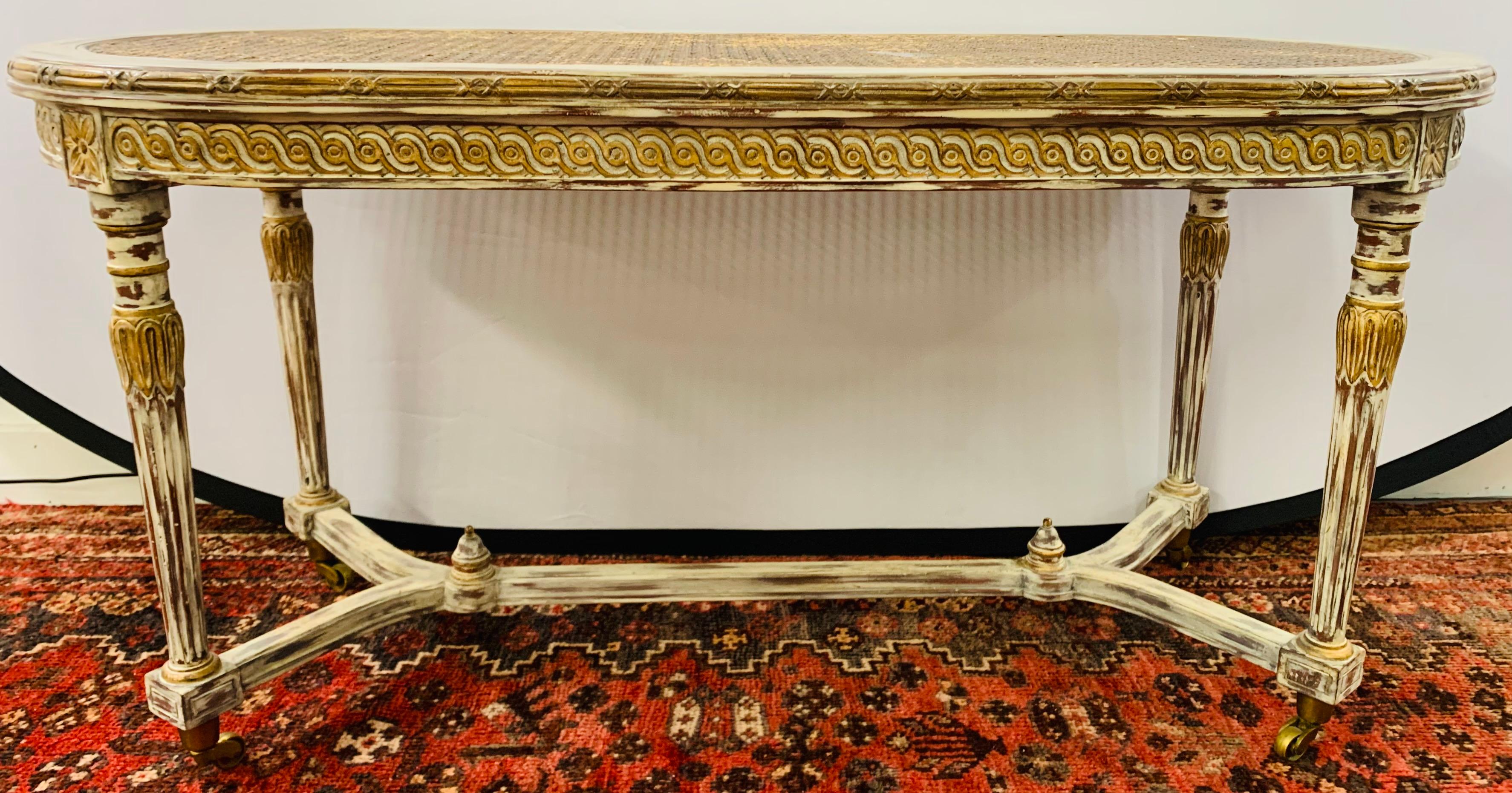 A stylish French Louis XVI style coffee table with wheels attributed to Henredon. The oval shaped table is hand painted in an antiqued white and features a caned table top all supported by fluted wheeled legs joined by a stretcher. The table top and