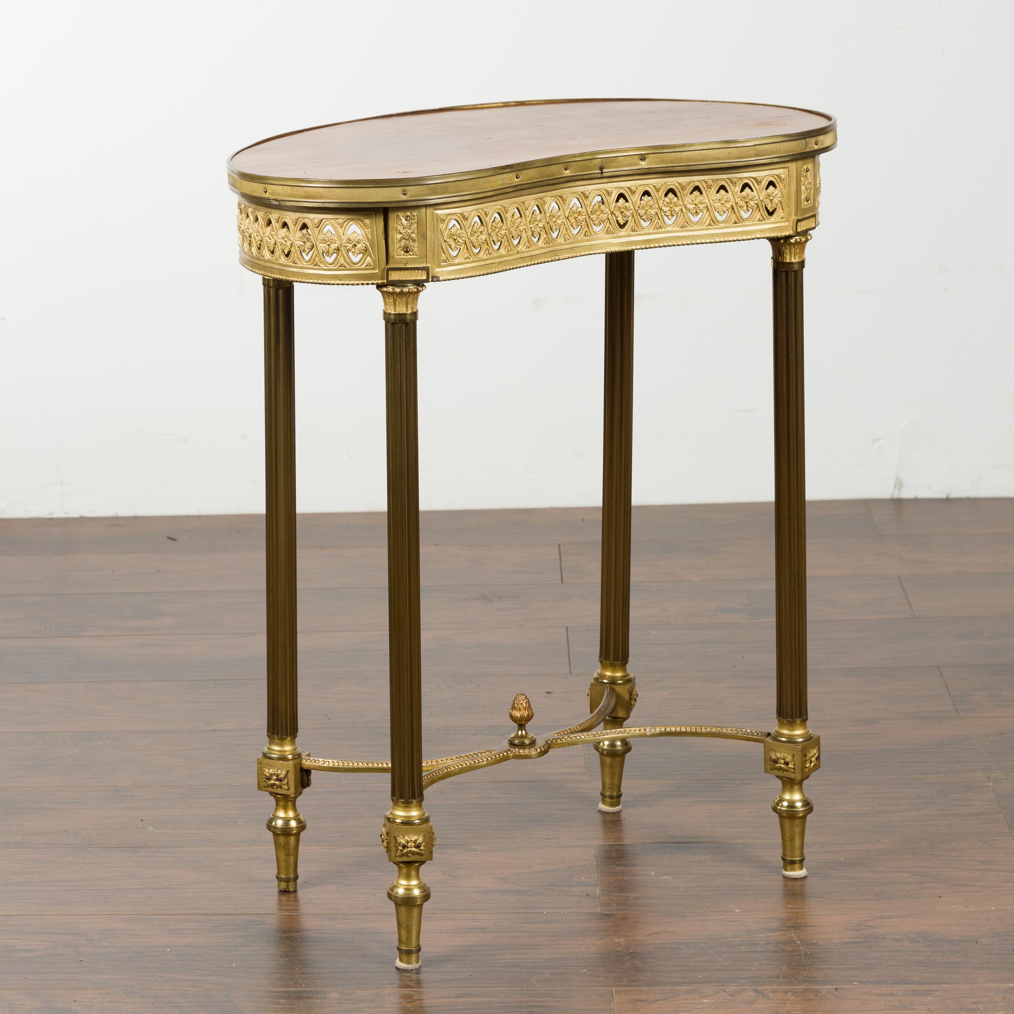 A French Louis XVI style kidney shaped gilt bronze accent table from the 19th century with fluted columns and rosettes. Created in France during the 19th century, this gilt bronze table features a kidney shaped wooden top with reeded rim, sitting
