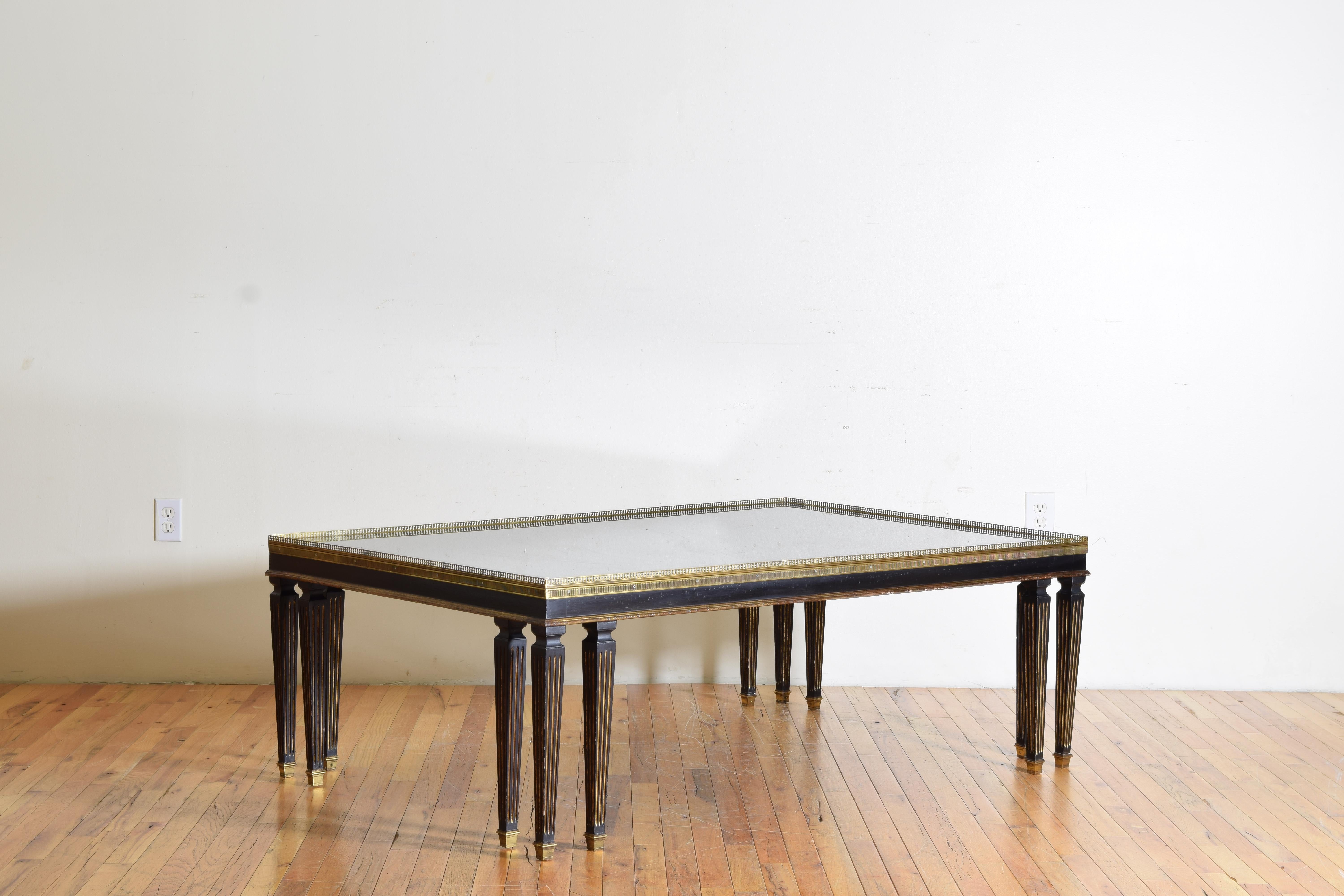 Having a large rectangular tinted glass inset top within a pierced brass gallery, the frame and legs of ebonized wood with gilded bands and details, raised on square tapering legs, each corner with three legs ending in square brass casters.