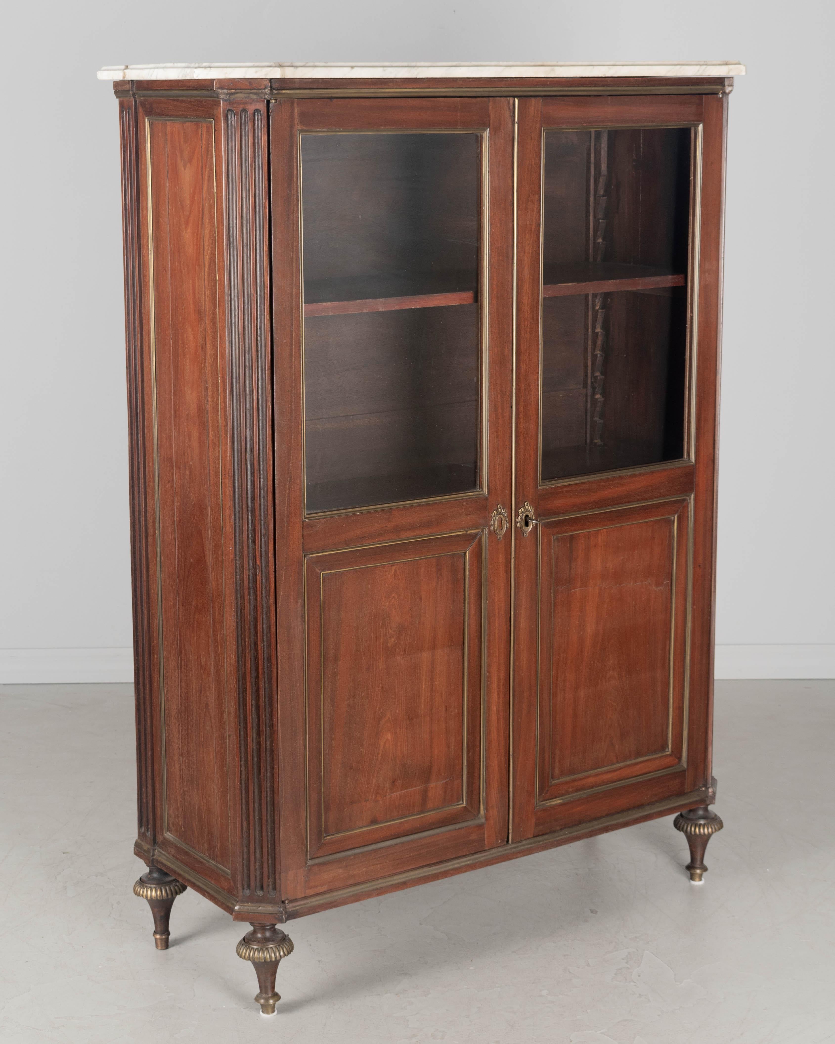 Una bibliotheque, o libreria, in stile Luigi XVI francese dei primi del Novecento con piano in marmo. Realizzato in legno massiccio e impiallacciato di mogano su Oak. Porte originali in vetro soffiato con scuretti decorativi in ottone, serratura e