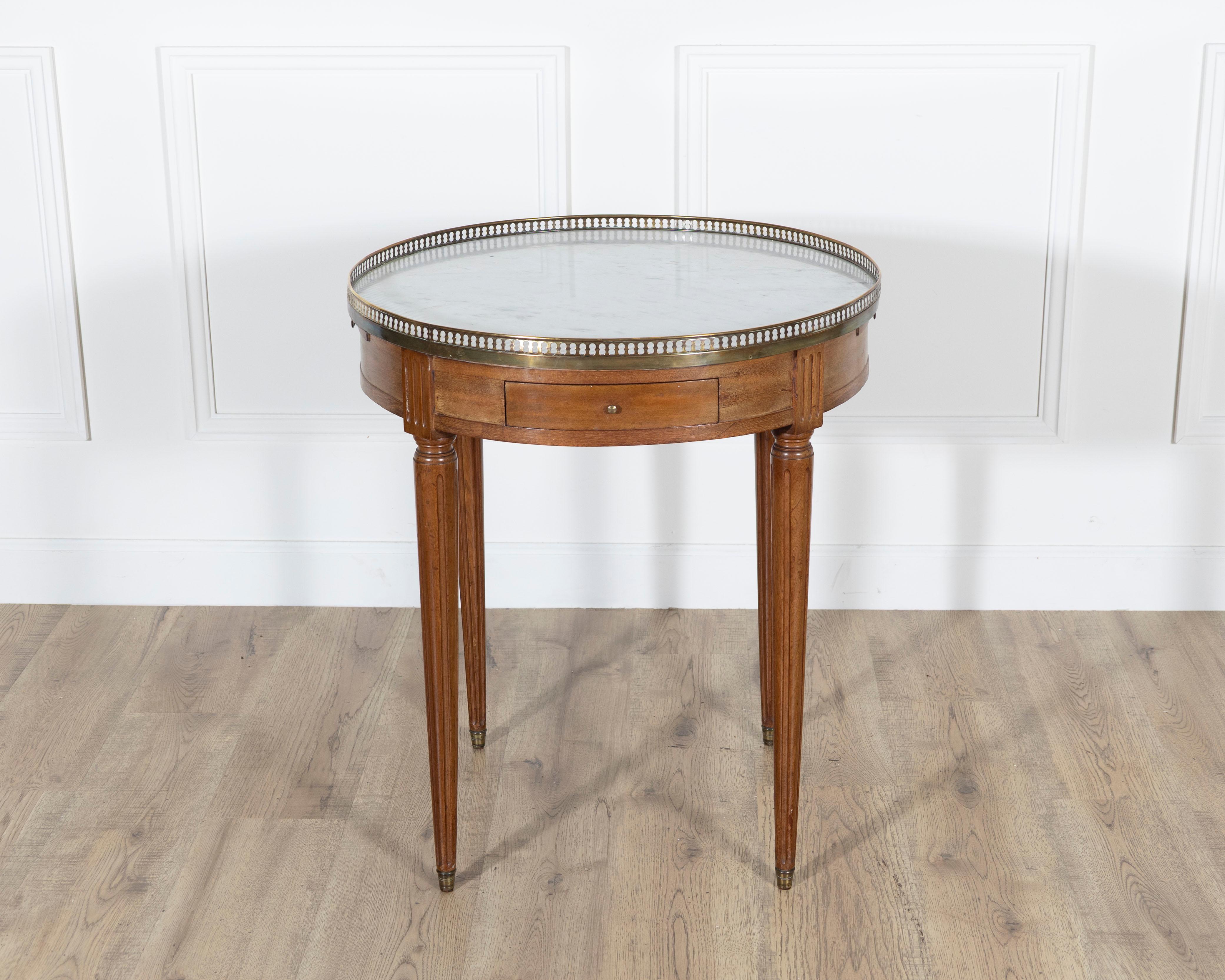 Elegante mesa bouillotte de estilo Luis XVI procedente de Francia, de finales del siglo XIX, finamente elaborada en caoba con refinados detalles neoclásicos. El faldón circular está equipado con dos cajones y dos guías extraíbles forradas de piel,
