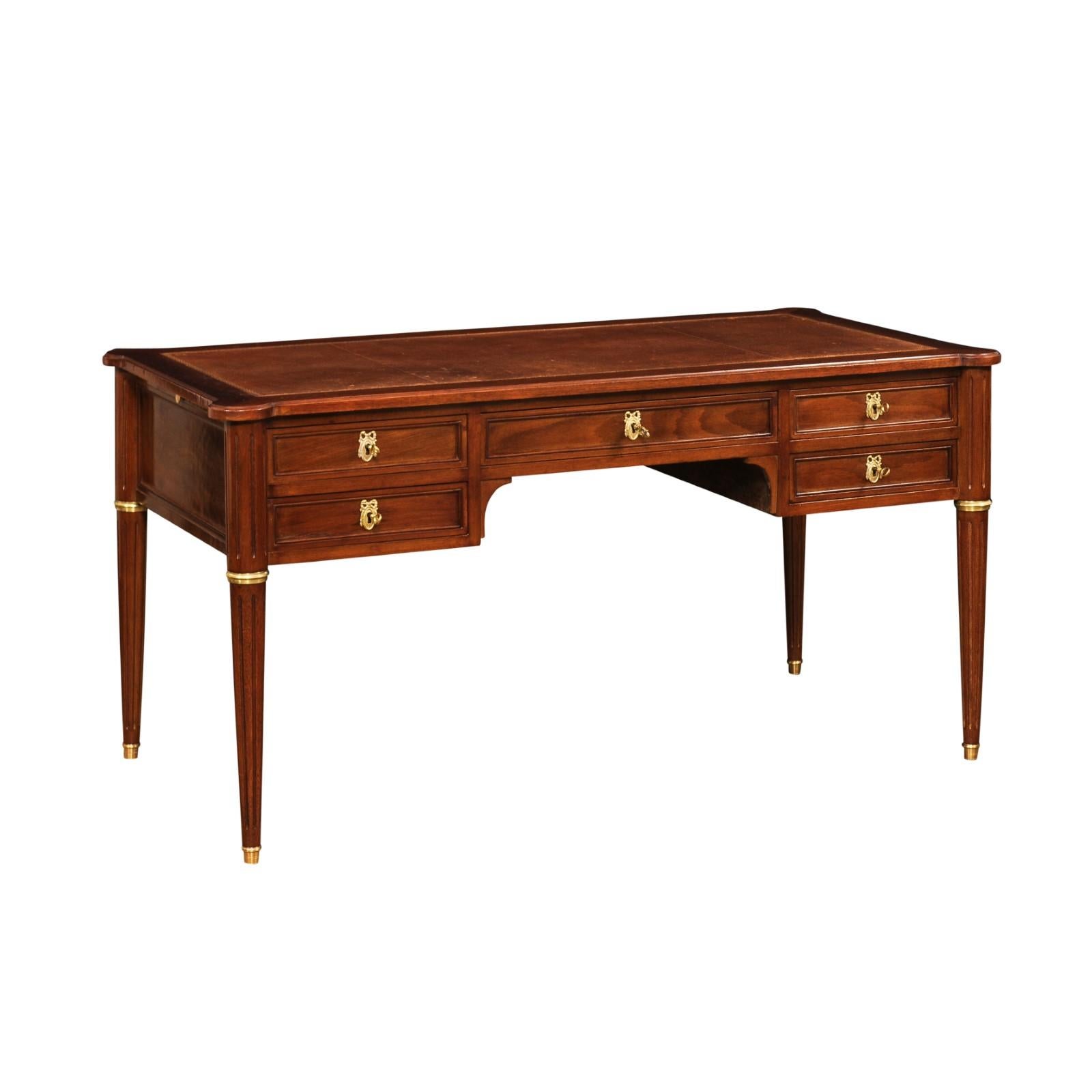 A large Louis XVI style mahogany two-sided bureau plat desk from the 20th century with five frontal drawers, tan leather top and pull outs. Created in France during the 20th century, this mahogany desk features a tan colored leather top with rounded