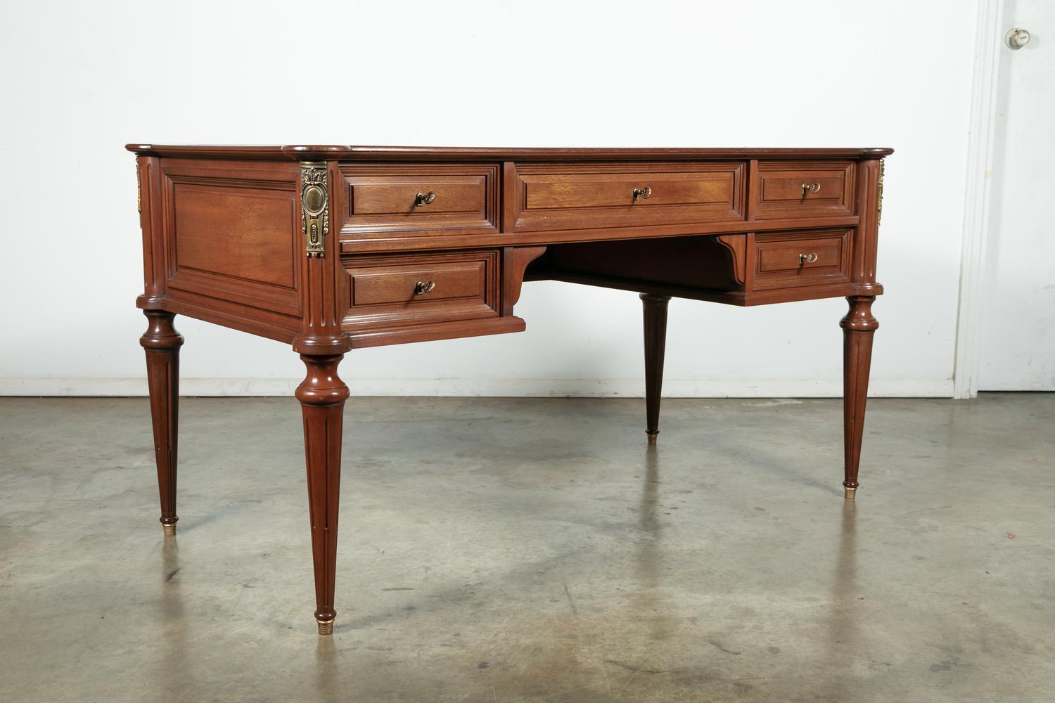 French Louis XVI style mahogany bureau plat or writing table with a cookie cutter top having an attractive cognac leather writing surface with beautiful gilt tooling framing the edges and bronze ormolu mounts, circa 1940s. A single central drawer is
