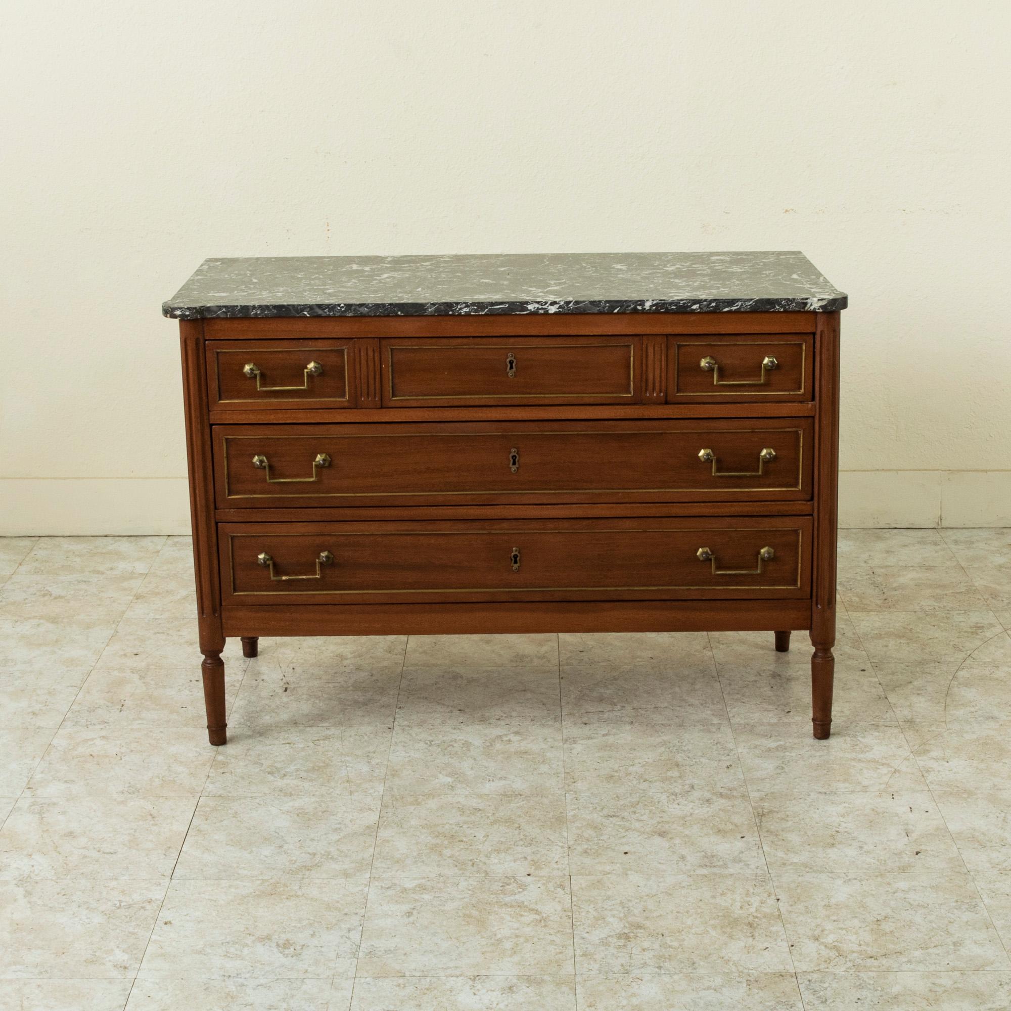 This French Louis XVI style mahogany commode or chest of drawers features a beveled Saint Anne marble top and fluted rounded corners. Its three drawers of dovetail construction are detailed with bronze banding and are fitted with their original