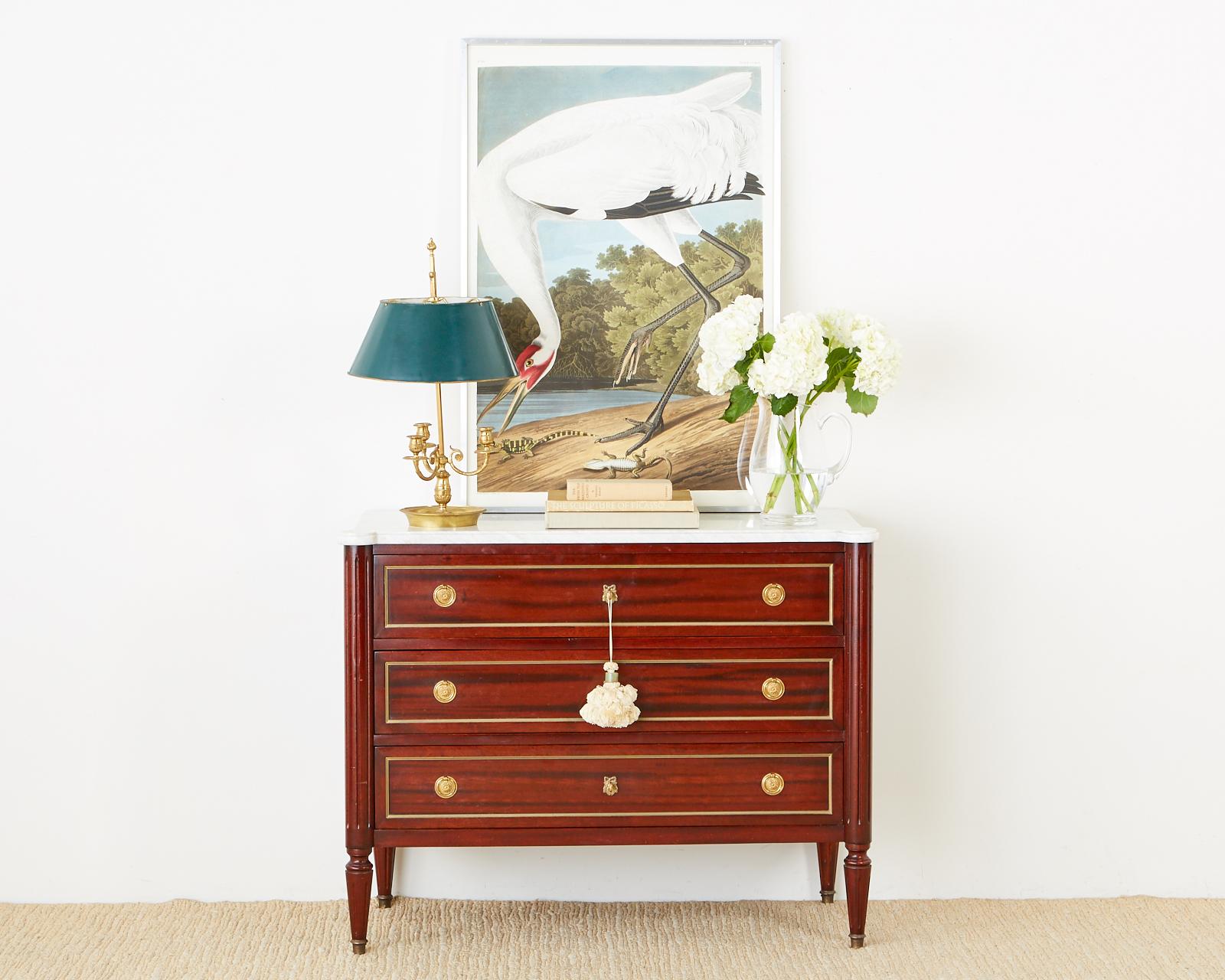 Fine French mahogany commode, chest of drawers, or dresser featuring a dramatic conforming Carrara marble top. The beautifully crafted case is fronted by three large storage drawers with bronze trim and brass pulls. Each side is pilastered with a