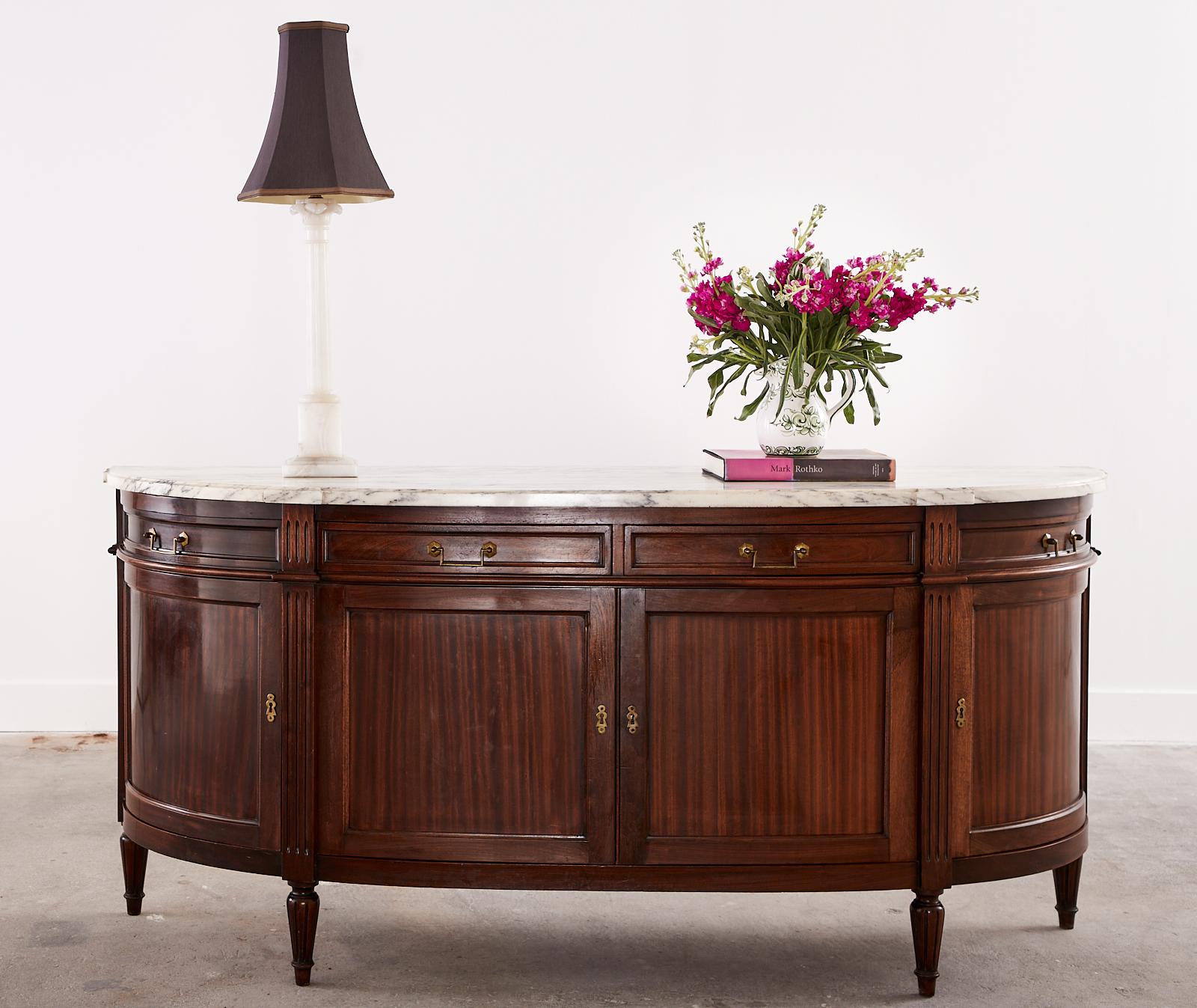 Classic French mahogany sideboard or buffet featuring a 1 inch thick Italian Carrara marble slab top. Beautifully crafted in the grand French Louis XVI taste. The case has gracefully curved demilune ends with reeded column pilasters on the front and