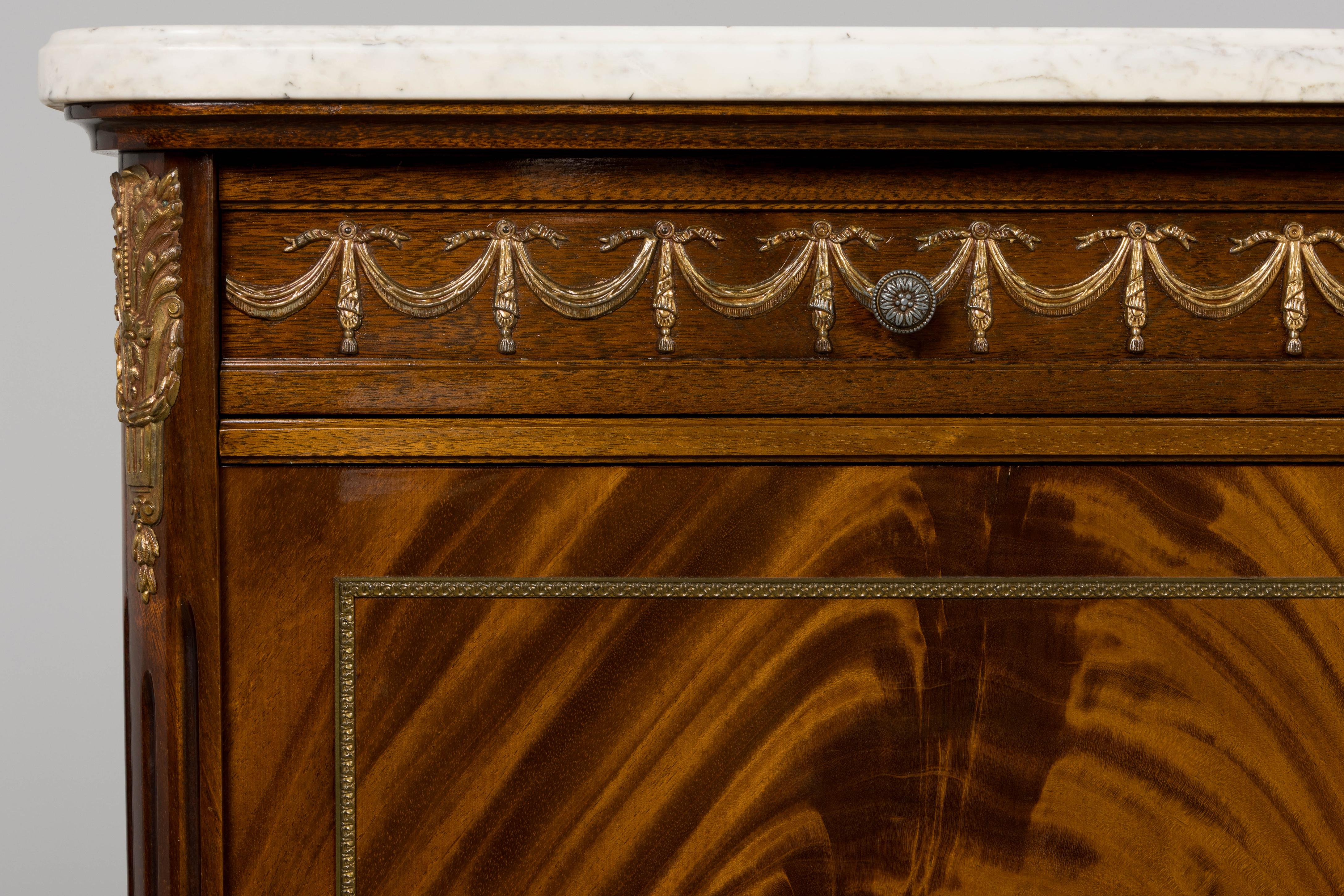 A substantial mid-20th century sideboard made in the grand Louis XVI style, sourced from Provence, France. Crafted with richly figured mahogany veneers and crowned with an impressively heavy Carrara marble top, this piece combines refined