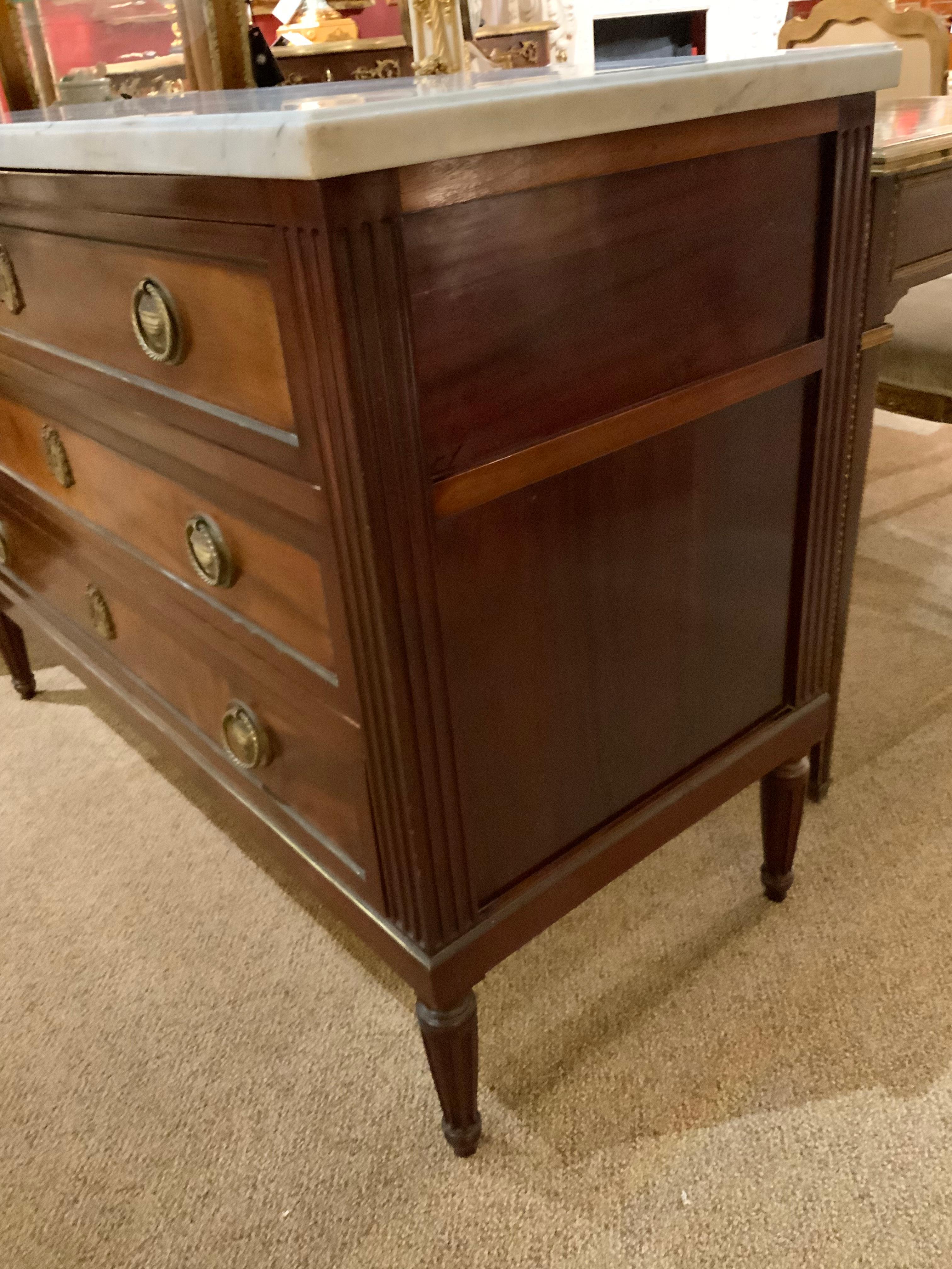 French commode with white marble top with pale gray veining. Three drawers with bronze pulls.
The commode is rising on tapered fluted legs. Brass banding around the drawers adds design 
Interest.