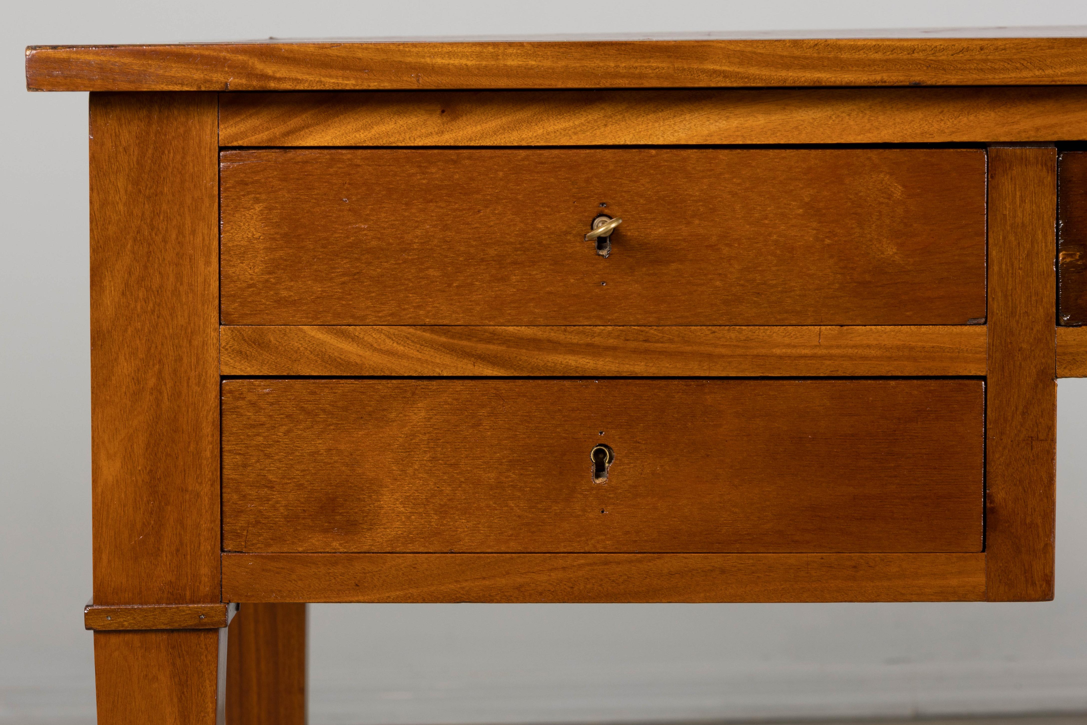 A large French writing desk or library desk in the Neoclassical Louis XVI style, sourced from Provence, France. Expertly hand-crafted from solid mahogany, the desk features a rectangular top inset with burgundy red tooled leather, flanked by two