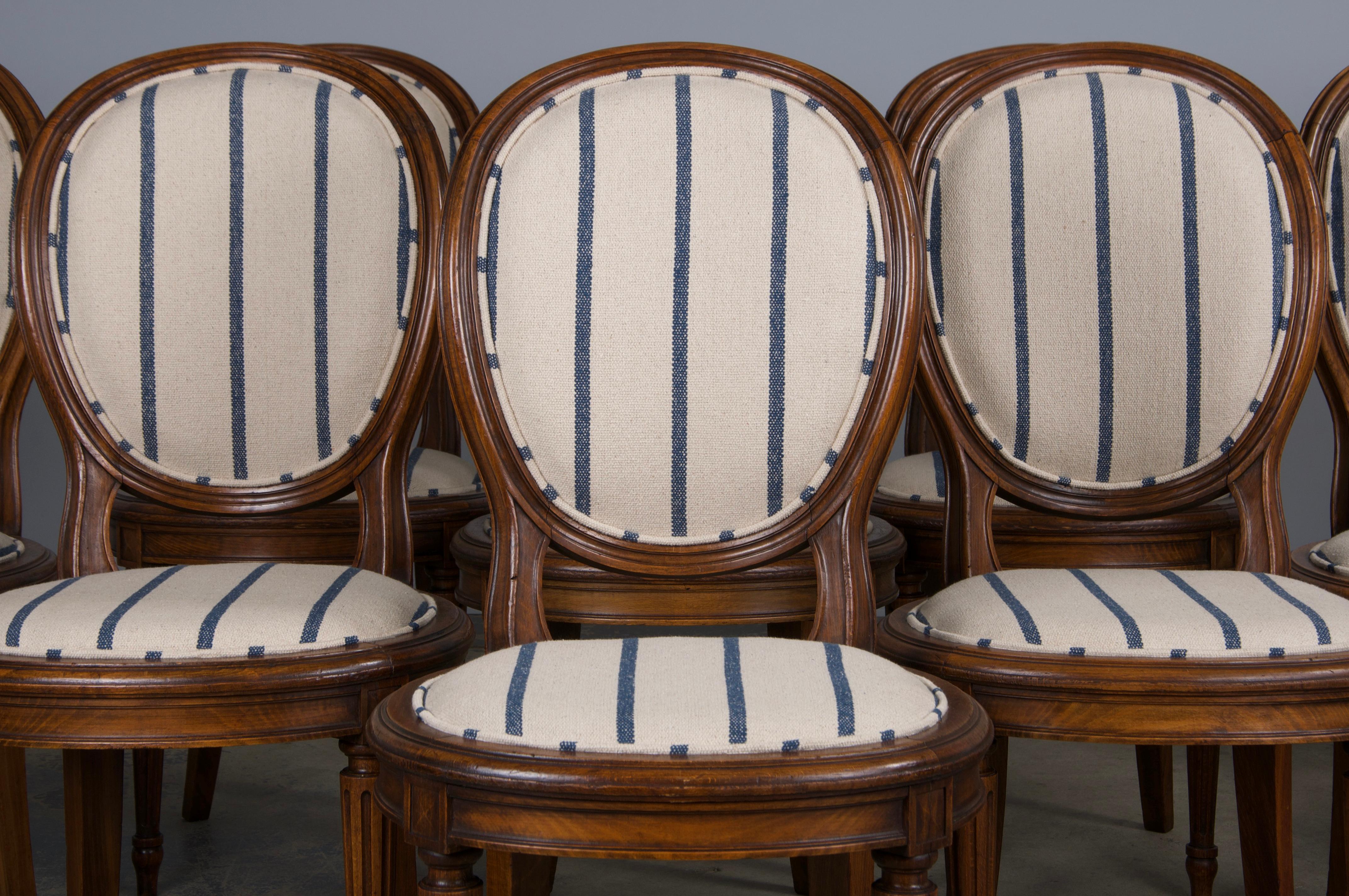 An exquisite set of twelve early 20th-century French dining chairs in the Louis XVI style, sourced from Provence, France. Each chair features a hand-molded, oval-shaped medallion back frame crafted from solid maple wood. The chairs have been