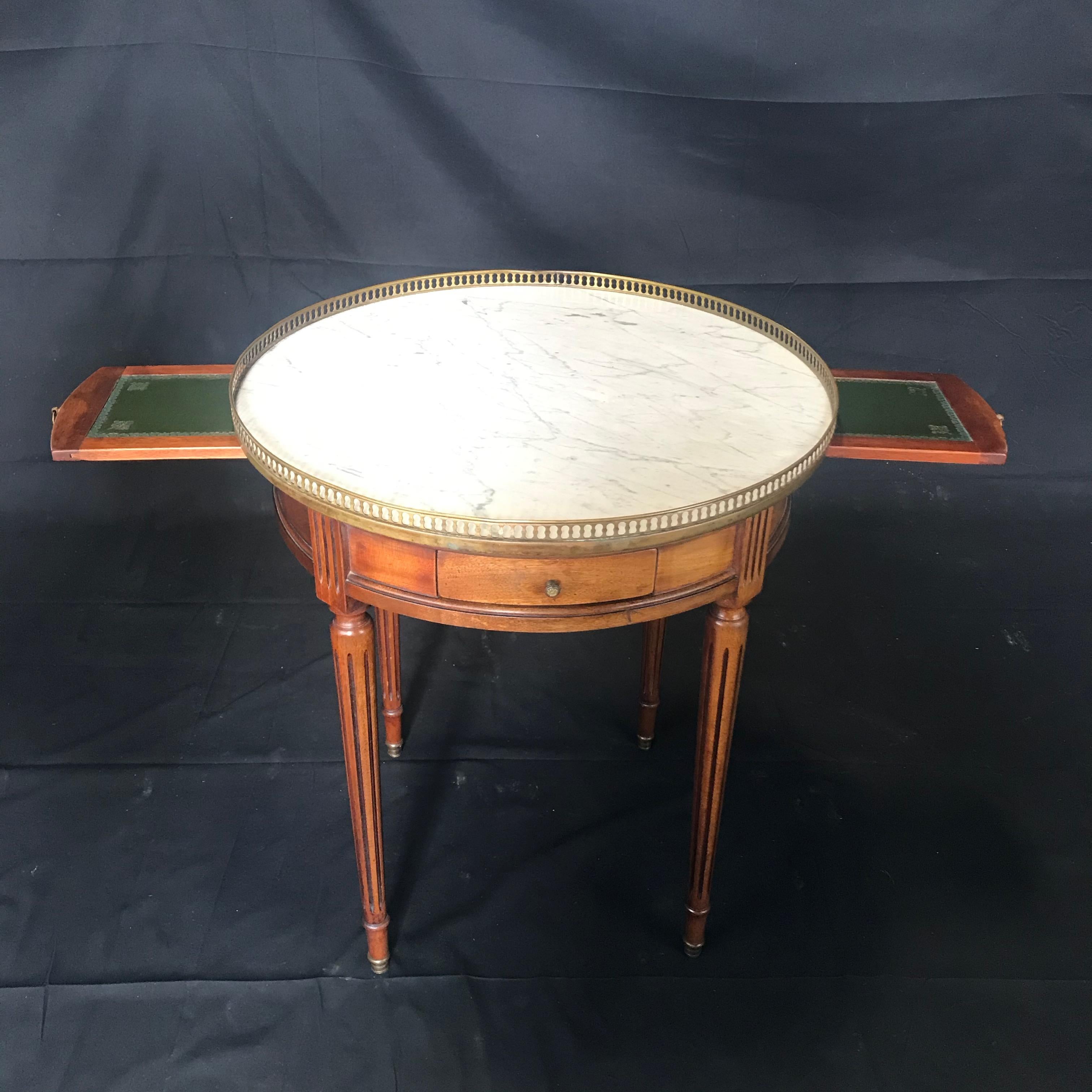 Distinctive French bouillotte walnut table featuring a round white marble top made in the Louis XVI style. The round case has two drawers and two pull outs on each side. The marble top has a brass gallery edge and is supported by elegant, tapered