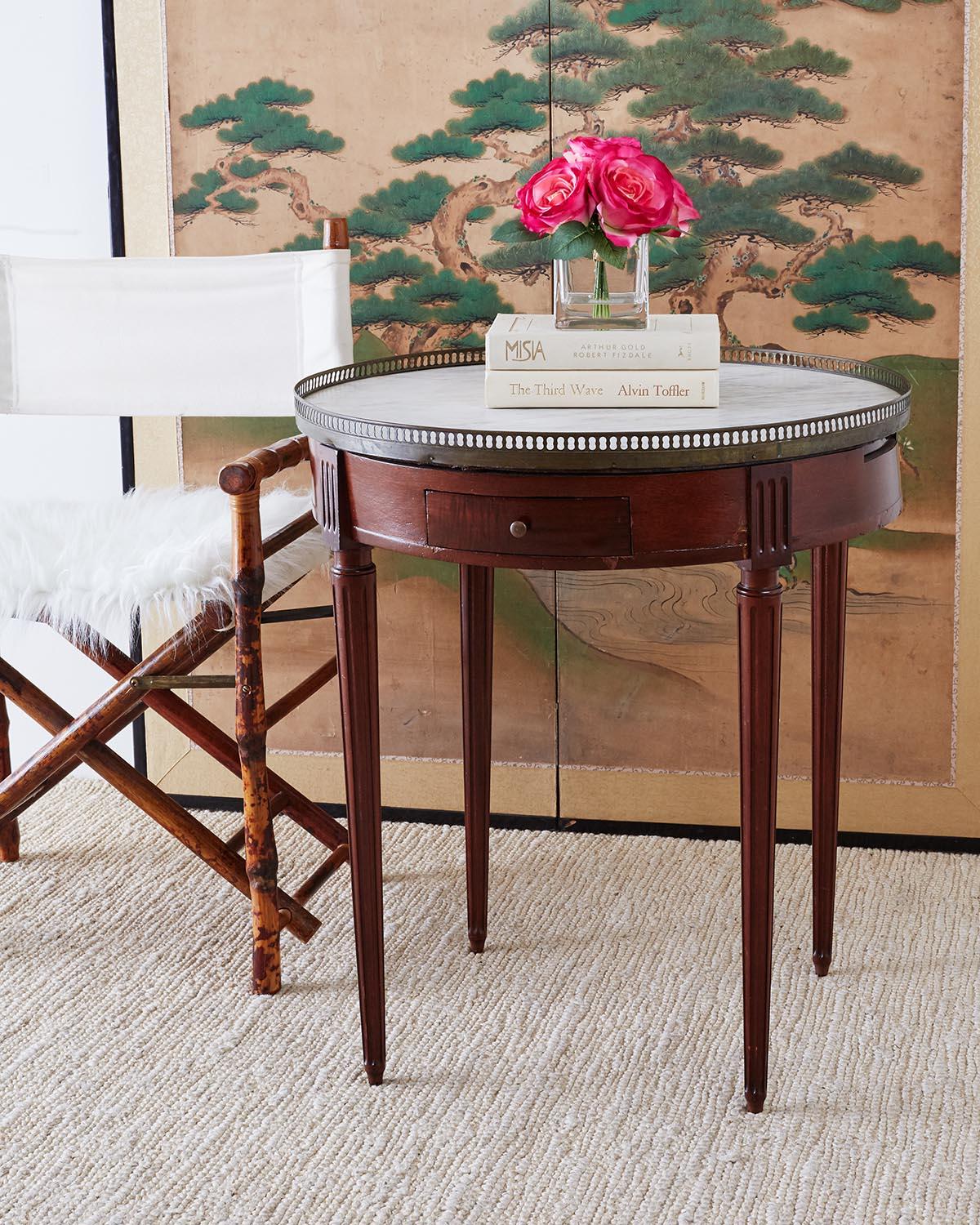 Distinctive French Bouillotte table featuring a round white marble top made in the Louis XVI taste. The round case has two drawers and two pull outs on each side. The marble top has a brass galleried edge and is supported by elegant, tapered legs.