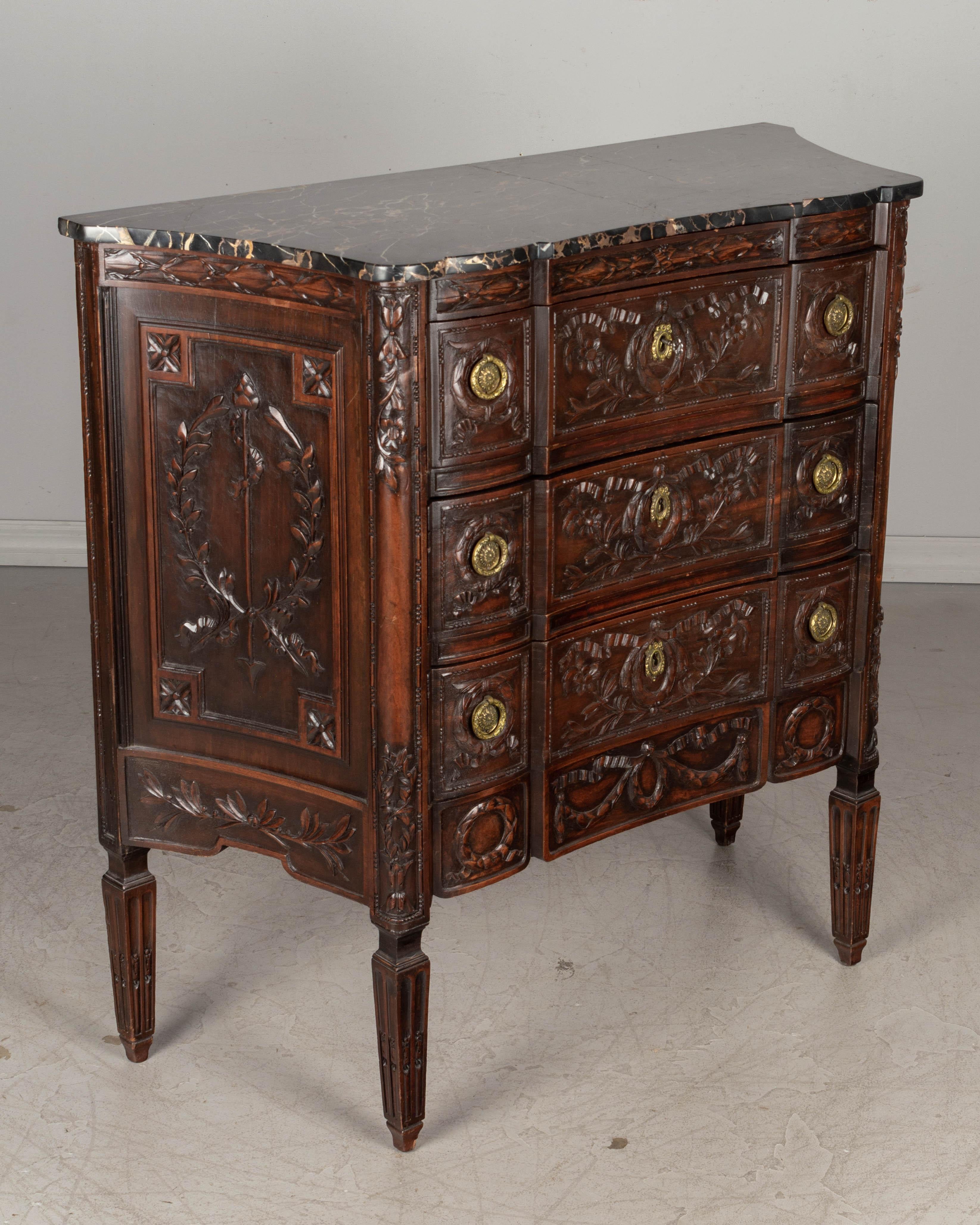 A Louis XVI style French marble top walnut commode with three dovetailed drawers and curved sides. Heavily carved decoration and original brass hardware with one key. Veined marble top has been repaired. Waxed patina. Please refer to photos for more
