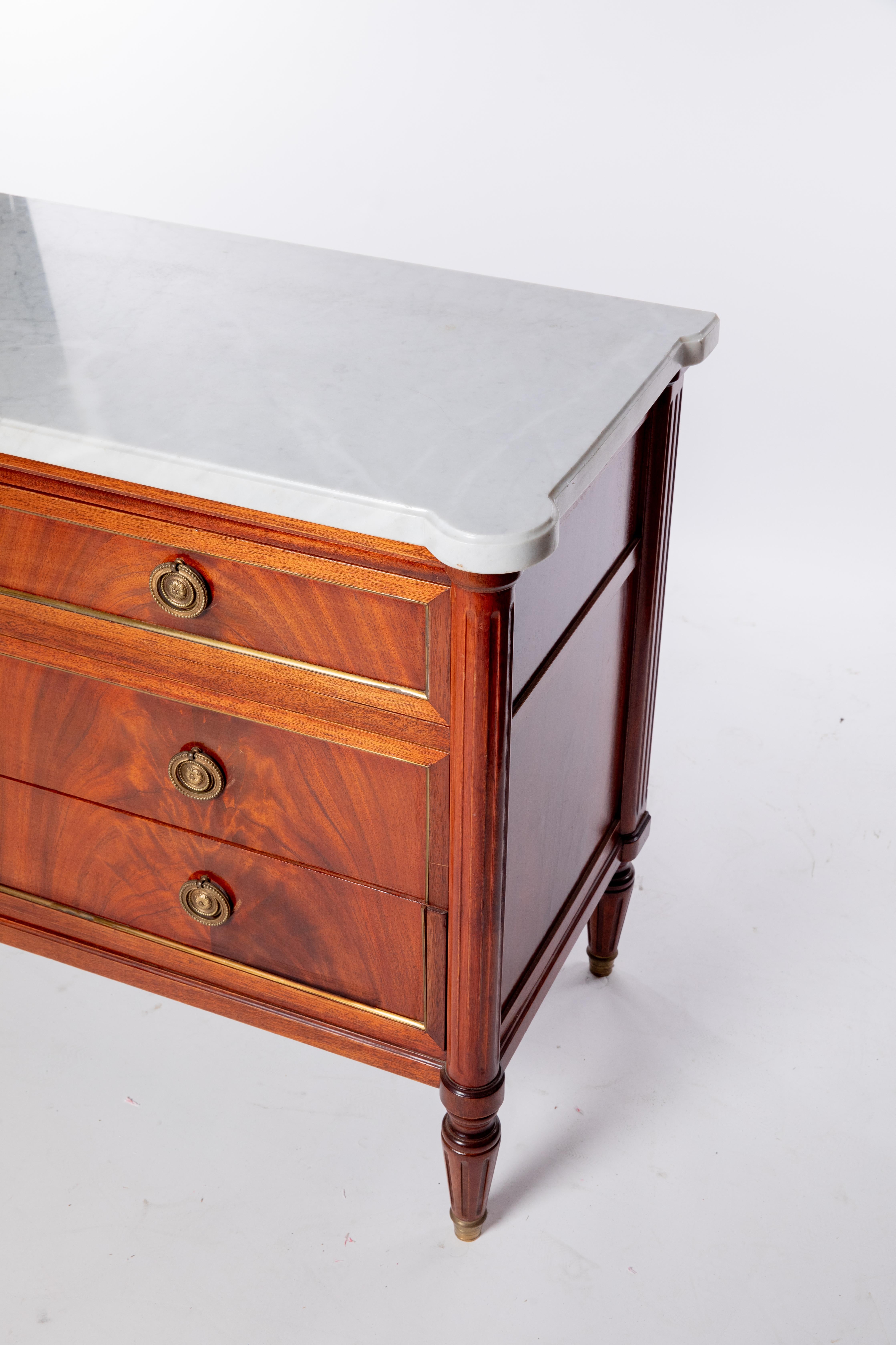 French Louis XVI style marble-top mahogany commode, 19th c., shaped marble top, over case fitted with four drawers, flanked by fluted corner posts, on tapered fluted legs, ending in metal-capped feet.