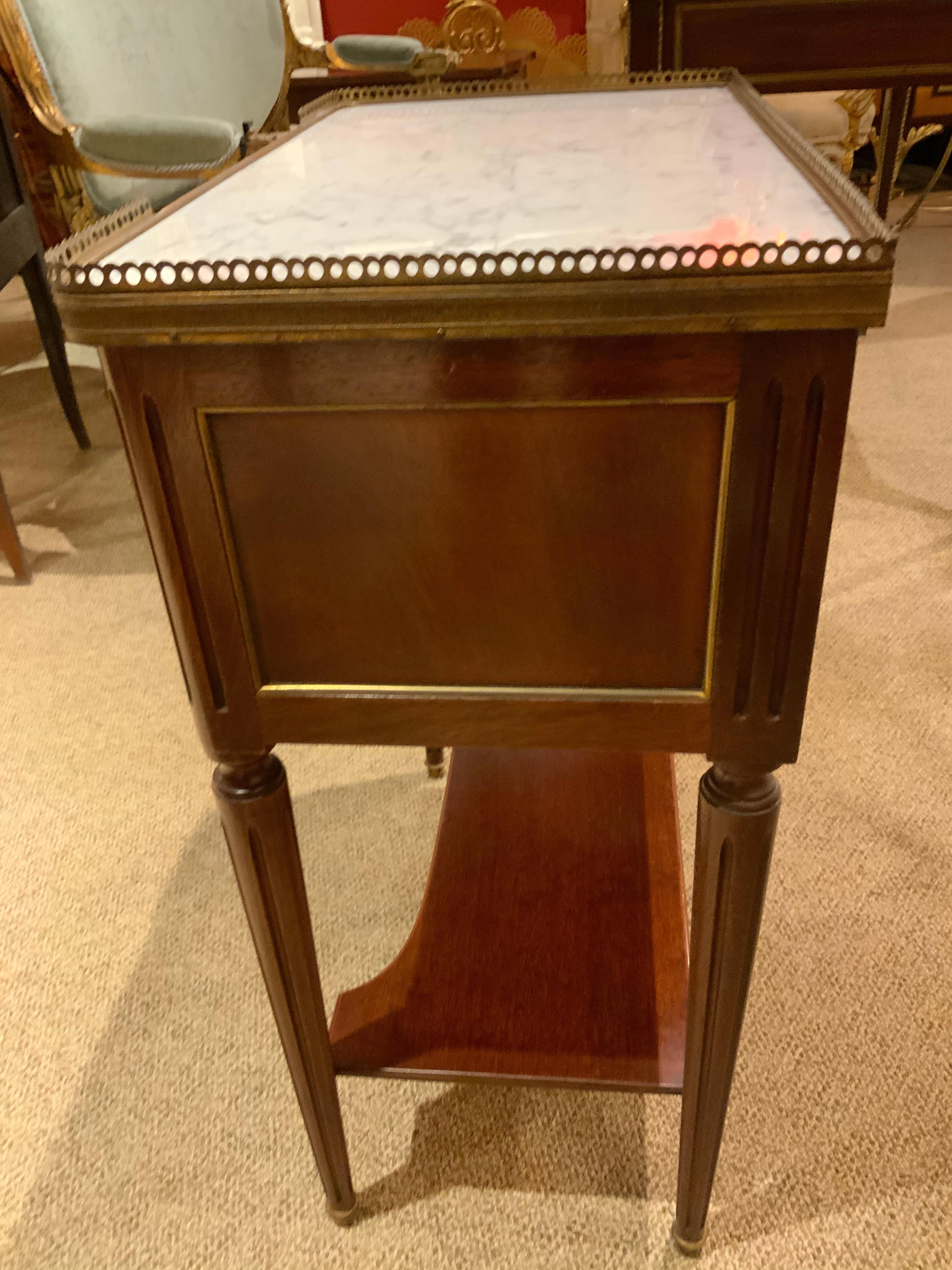 French Louis XVI style marble-top side table, late 19th century, pierced gilt metal gallery enclosing a marble top,
Seated on rectangular frame having two drawers with gilt metal trim, pulls and applied escutcheons, shaped medial shelf, joined to