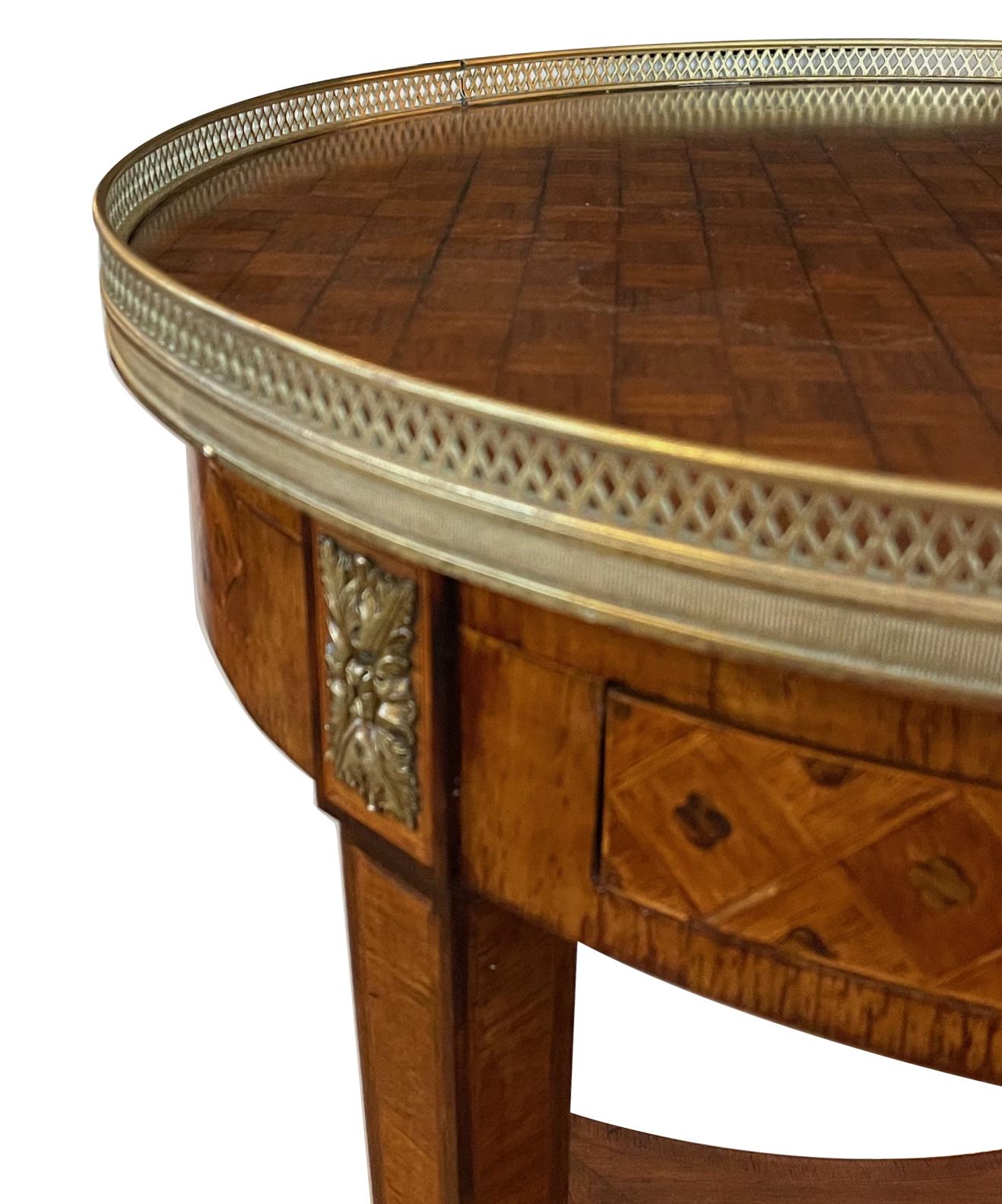 The circular top with brass pierced gallery over an apron fitted with two frieze drawers and candle slides; raised on tapering legs ending in bronze caps all joined by a lower concave shelf.