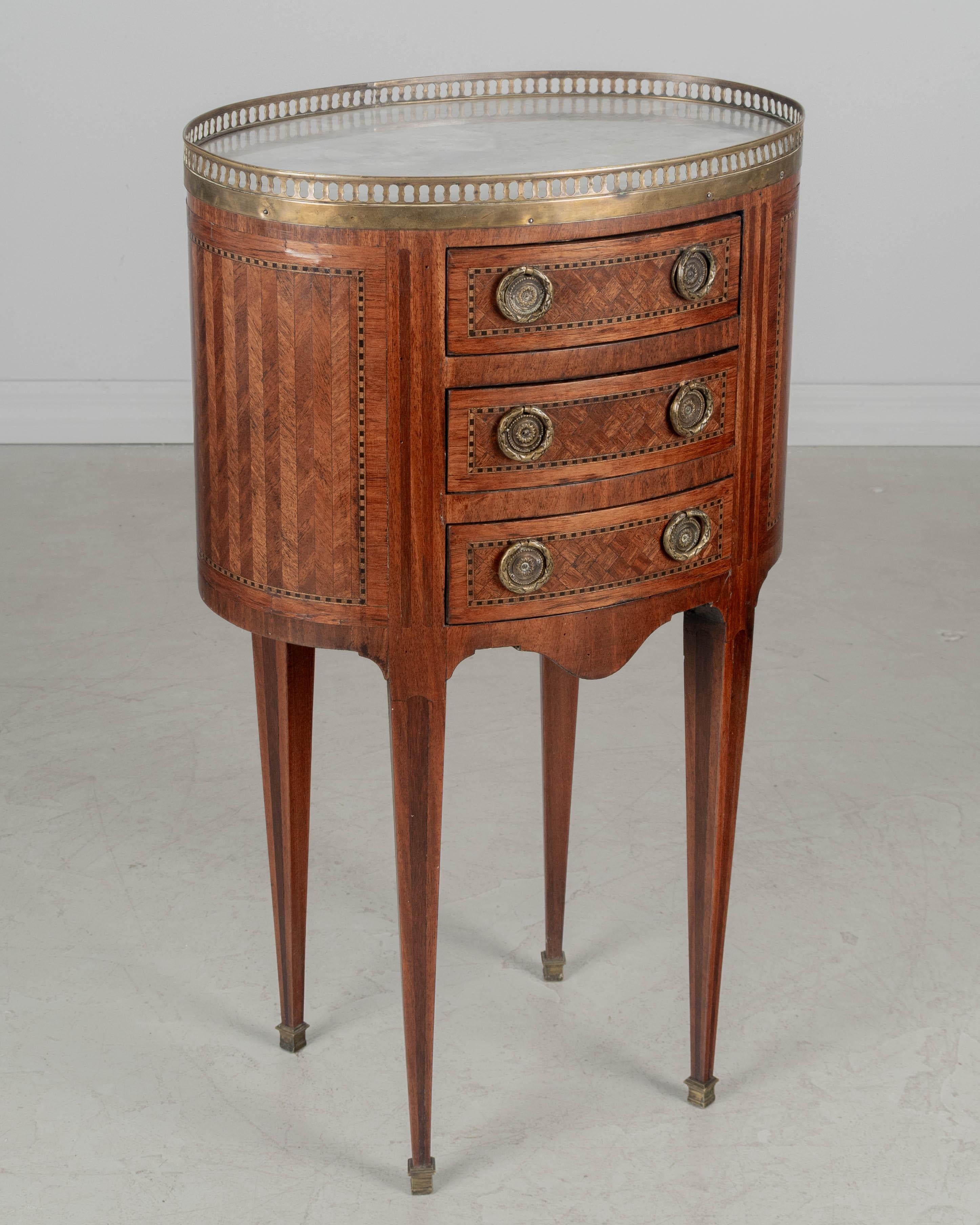Table d'appoint ovale en marqueterie de style Louis XVI français du début du XXe siècle, composée de placages d'acajou, de noyer et de tulipier et finie sur tous les côtés. Trois tiroirs à queue d'aronde avec poignées en laiton moulé. Pieds effilés