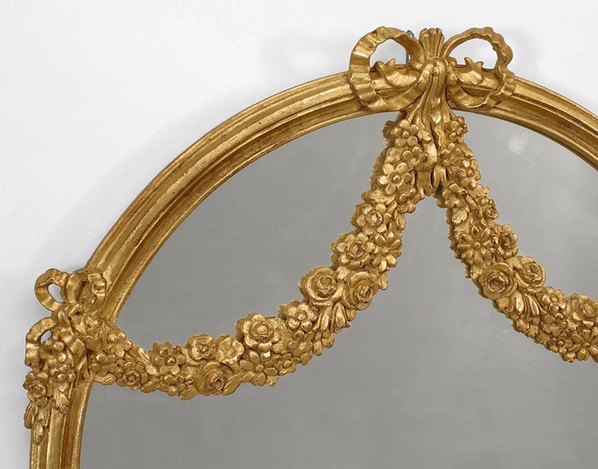 French Louis XVI-style (20th Century) giltwood wall mirror with two carved floral swags and arch design top with a bow knot.
